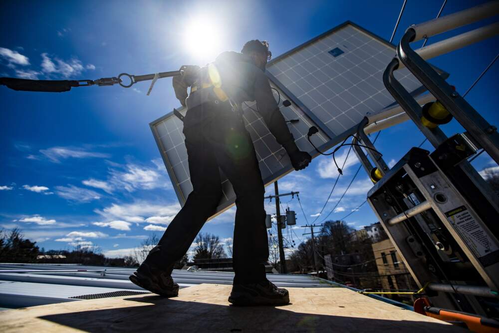 A technician removes a solar panel from a lift during a solar panel installation on the rooftop of Boston Building Resources in Jamaica Plain. (Jesse Costa/WBUR)