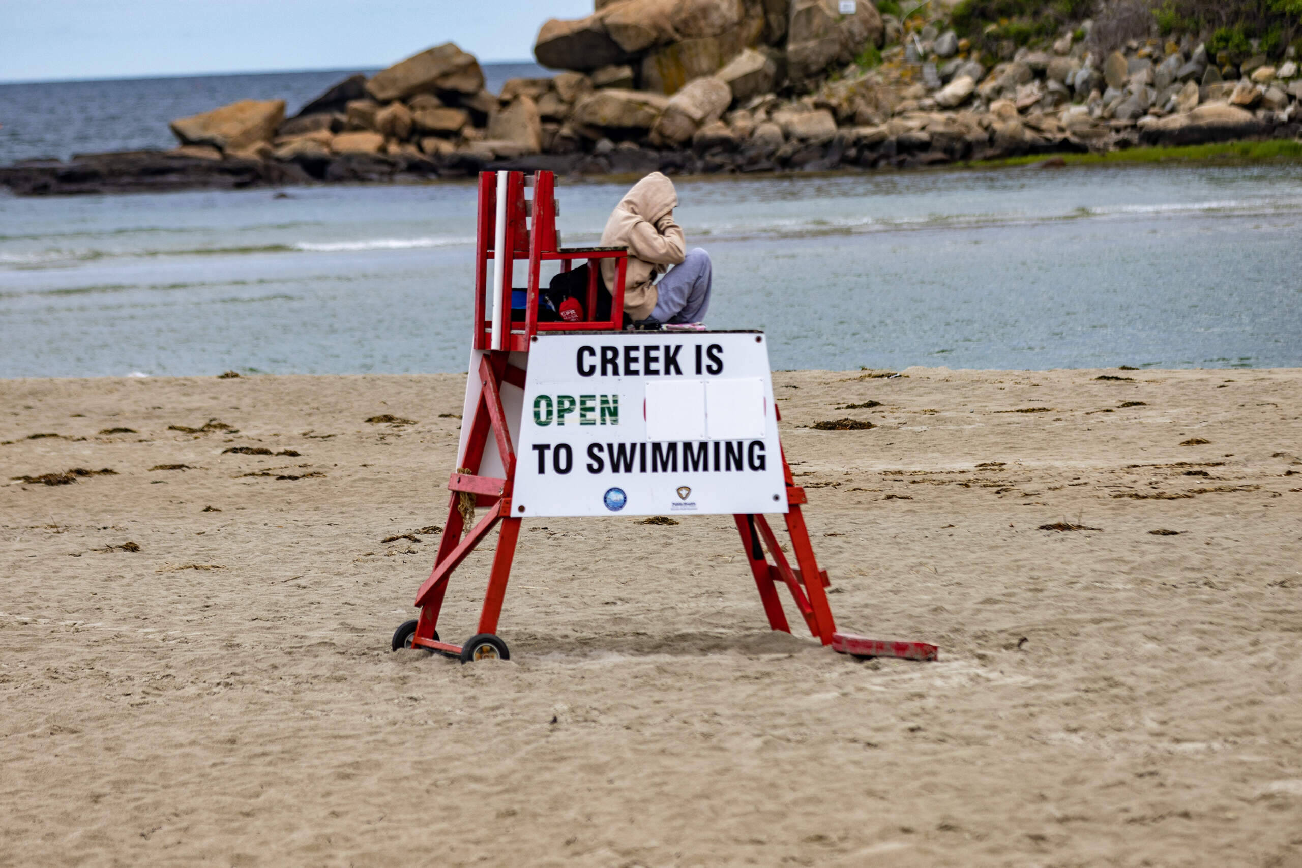 A lifeguard sits at their post at Good Harbor Beach in Gloucester with an adjustable sign mounted on the side of the chair indicating the creek is safe for swimming. (Jesse Costa/WBUR)