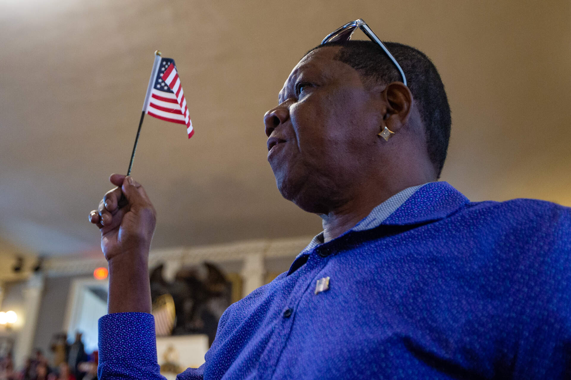 A naturalization applicant stands and waves a small American flag after hearing the name of his home country during a naturalization ceremony at Faneuil Hall. (Jesse Costa/WBUR)