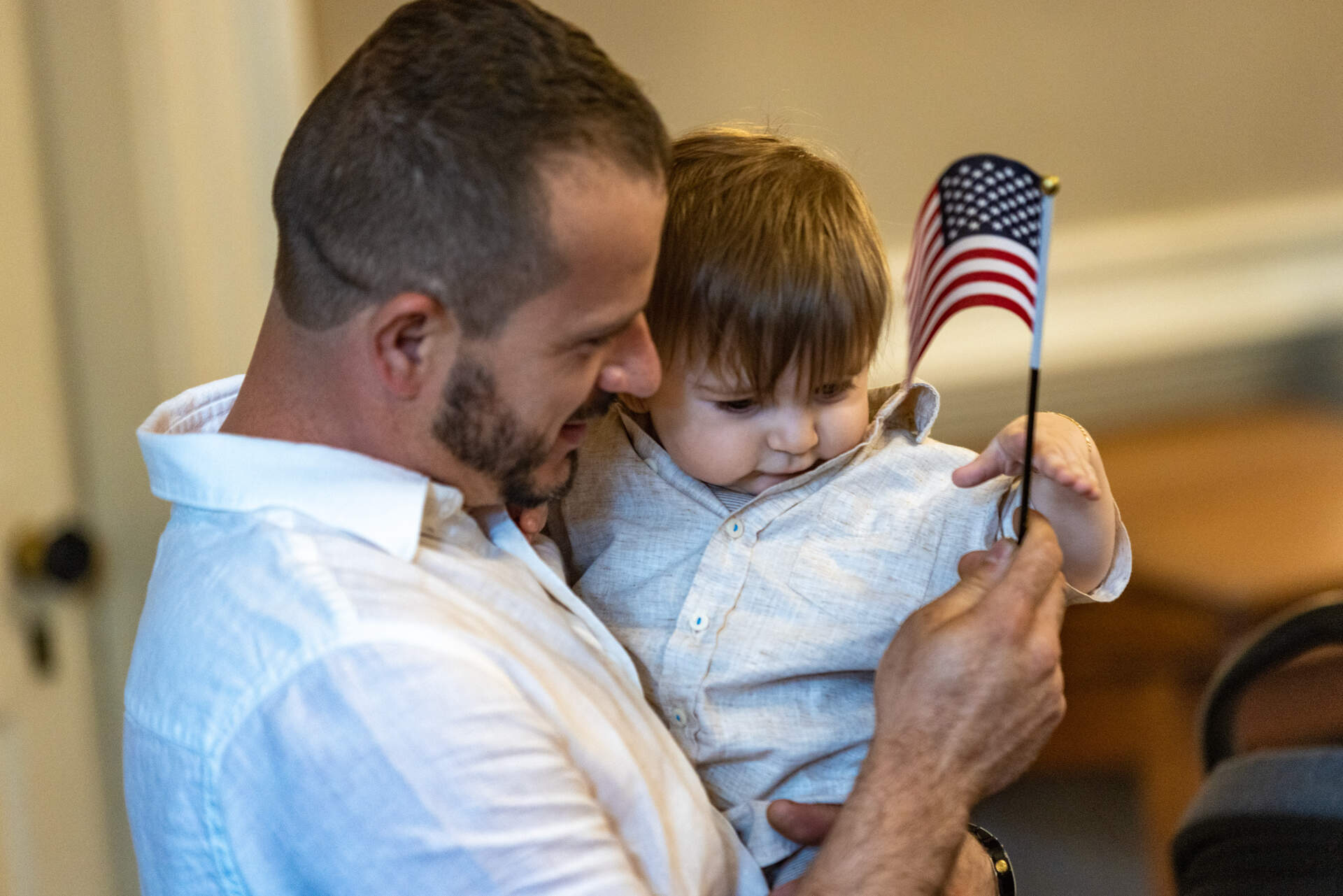 Parid Frakulla hands his 8-month-old son Dei Frakulla an American flag to wave during a naturalization ceremony at Faneuil Hall. (Jesse Costa/WBUR)