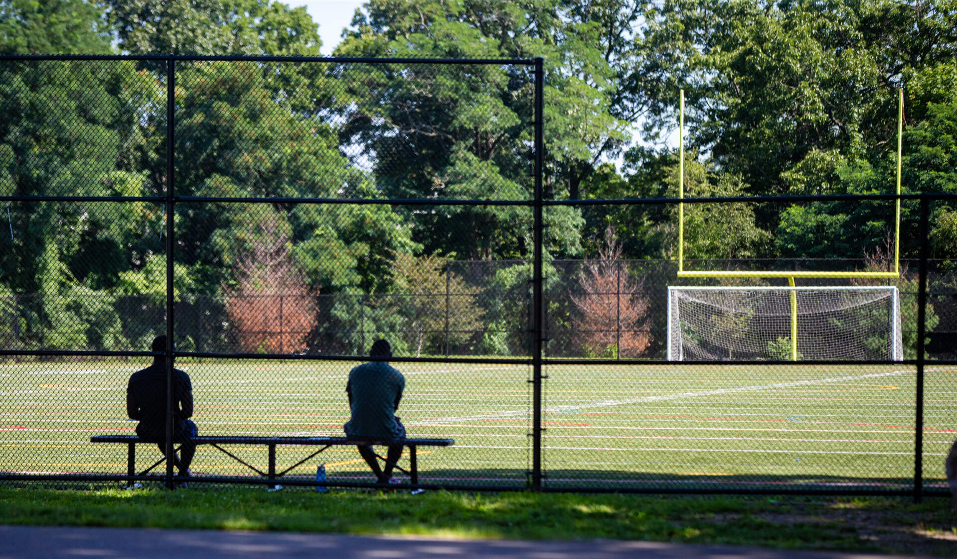 Two men sit on a shady bench in the football field at Reservation Road Park in Hyde Park. (Jesse Costa/WBUR)