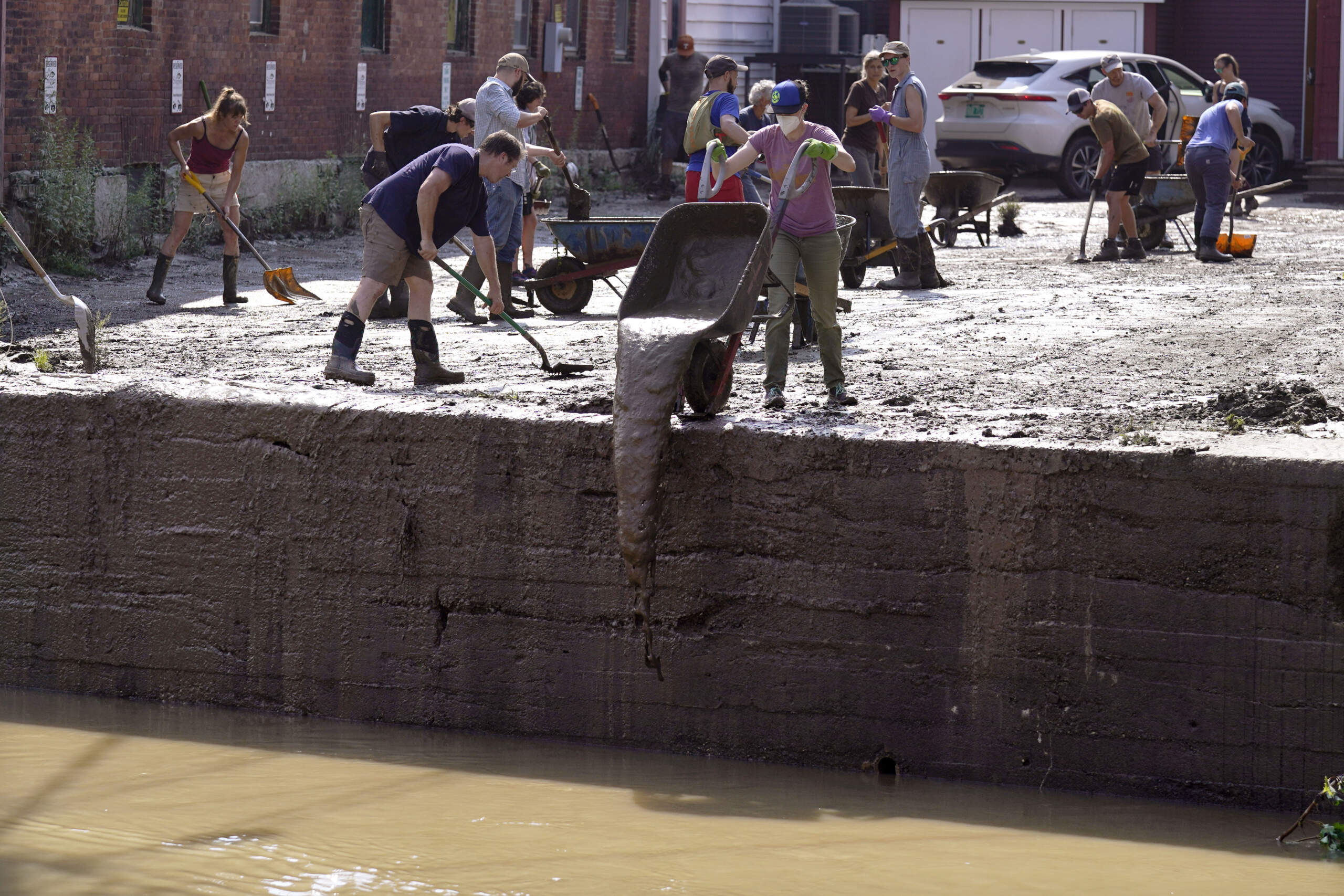 Volunteers clean up a downtown parking area on the banks of the Winooski River, Wednesday, July 12, 2023, in Montpelier, Vt. (Charles Krupa/AP)