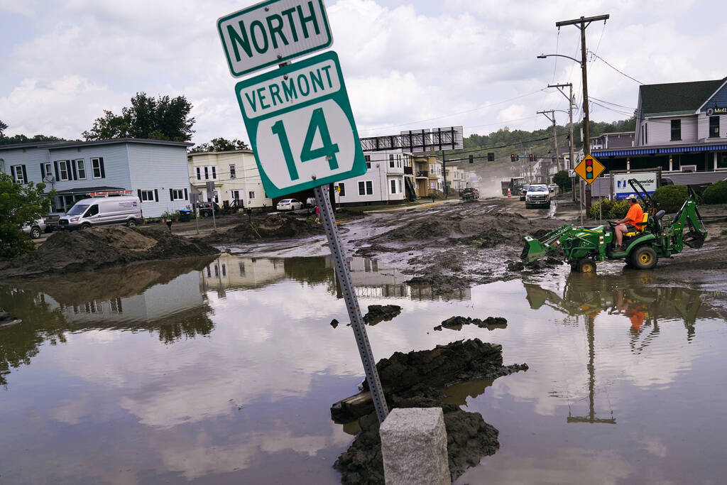 A small tractor clears water from a business as flood waters block a street on July 12, 2023, in Barre, Vermont. (Charles Krupa/AP)