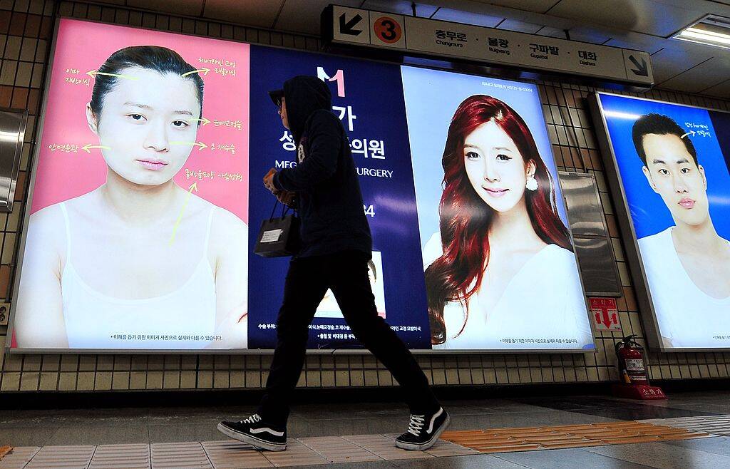 A pedestrian walks past advertisements for plastic surgery clinics at a subway station in Seoul on March 26, 2014. The South Korean capital Seoul is to restrict the use of plastic surgery adverts on public transport, officials said, after complaints that they were fuelling an unhealthy obsession with body image. AFP PHOTO / JUNG YEON-JE (Photo credit should read JUNG YEON-JE/AFP via Getty Images)