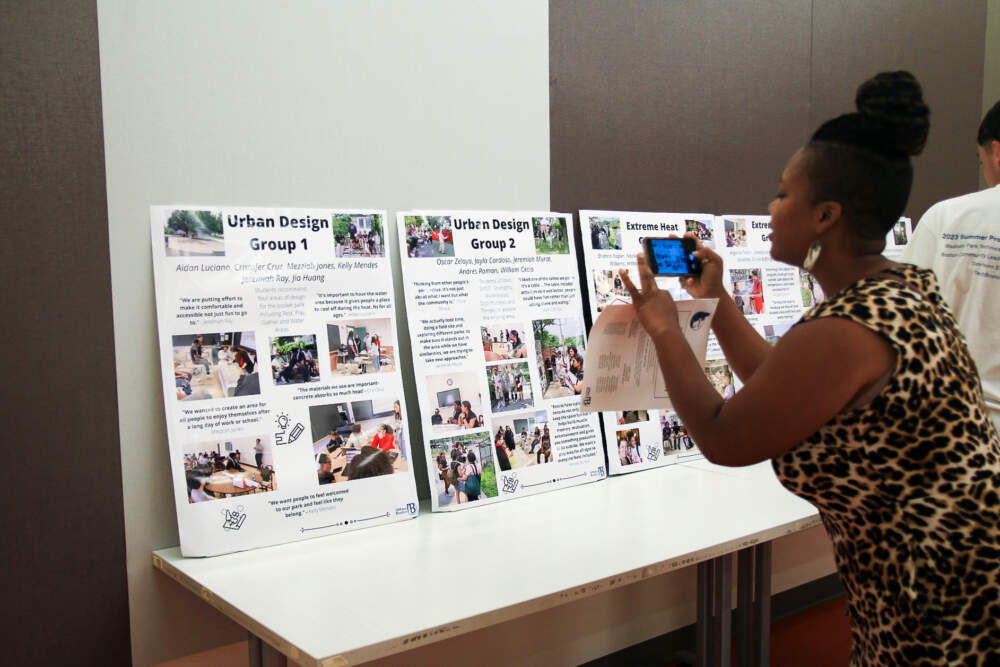 An attendee takes a photo of student presentation materials from the 2023 UMass Boston Summer Program in Urban Planning at Roxbury Community College. (Emily Piper-Vallillo/WBUR)