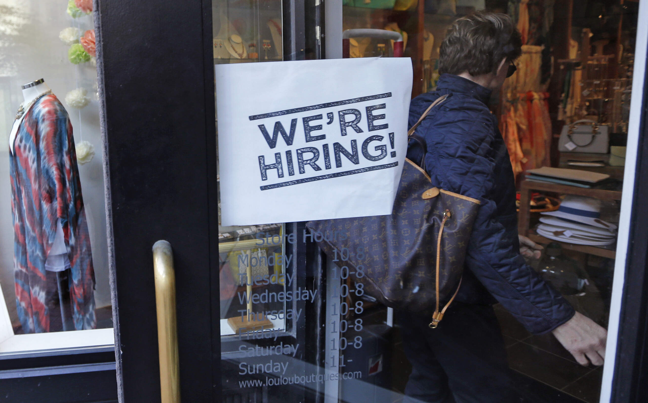 A woman passes a "We're Hiring!" sign while entering a clothing store in the Downtown Crossing of Boston, May 18, 2016. (Charles Krupa/AP)