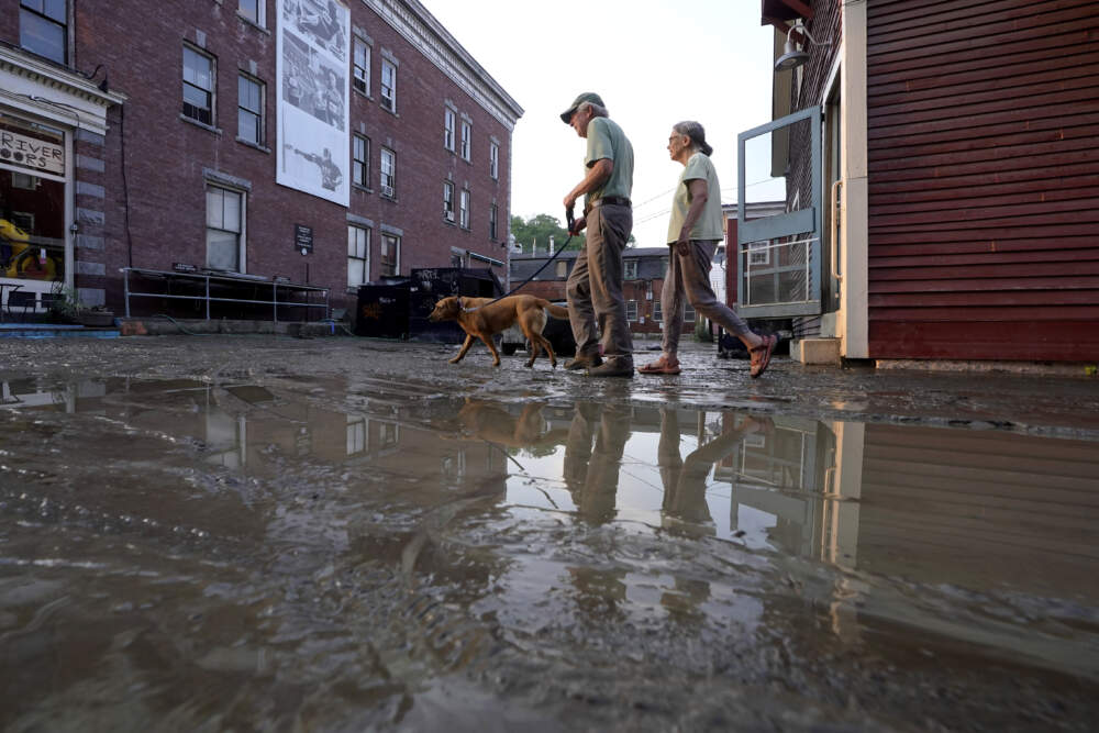 People walk a dog on a muddy street Tuesday, July 11, 2023, in Montpelier, Vt. A storm that dumped up to two months of rain in two days brought more flooding across Vermont on Tuesday. Flood waters from Vermont are now making their way down to Massachusetts through the Connecticut River. (Steven Senne/AP)