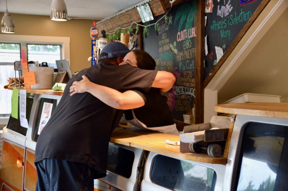 Rachel Karner hugs a patron at Goodman's American Pie. The restaurant was giving out free pizza on Wednesday to anyone in town who was helping with flood clean up. Karner says she used to work at the restaurant years ago and is now a local art teacher. "But I have the summer off and knew they'd need help, so here I am. I am so proud of this restaurant and so proud of this community." (Nina Keck/Vermont Public)