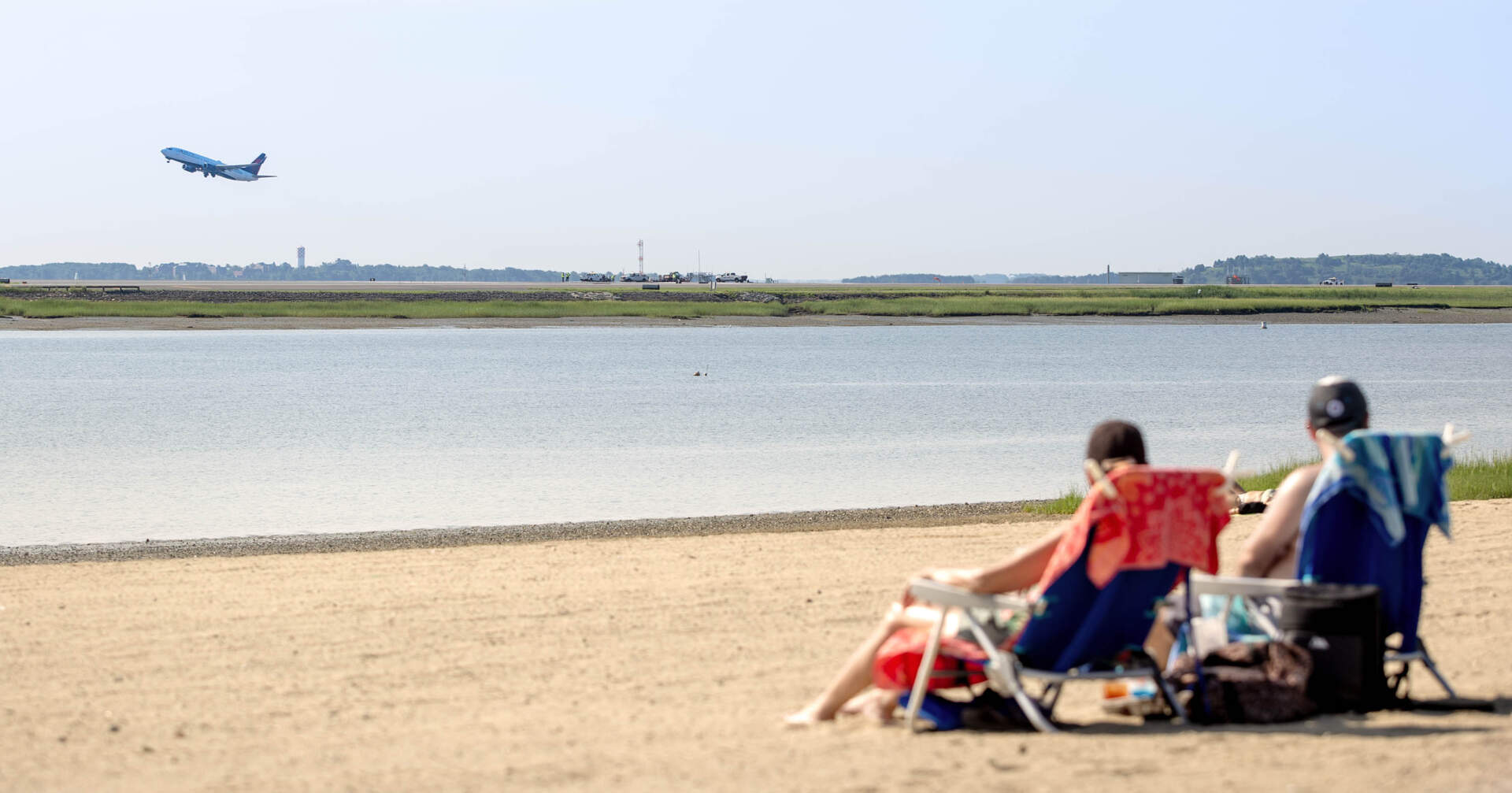 Beachgoers enjoy the sunshine on Constitution Beach in East Boston, as a plane takes off from Logan Airport. (Robin Lubbock/WBUR)