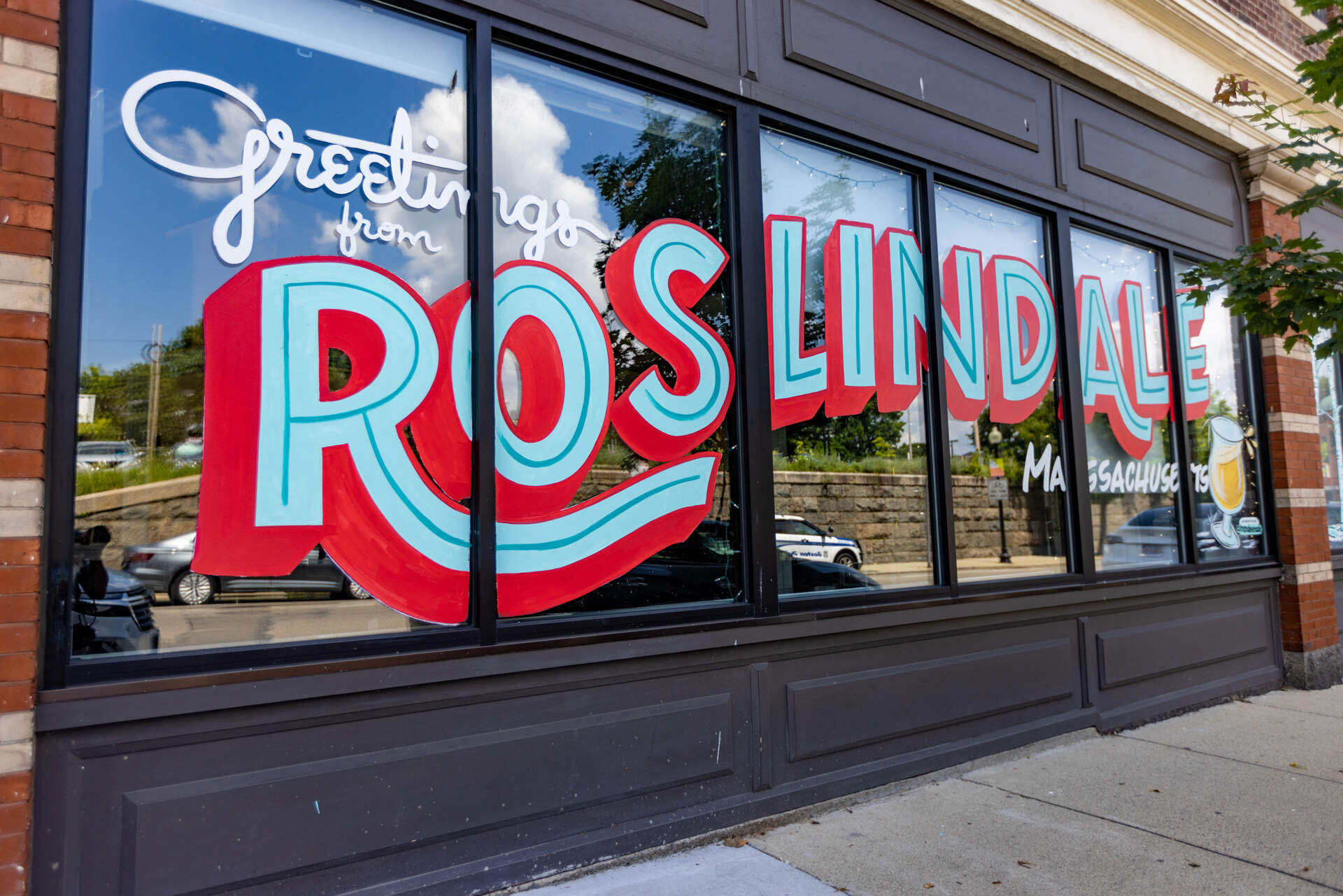 &quot;Greetings from Roslindale, Massachusetts&quot; is painted on the storefront of Distraction Brewing Company in Roslindale. (Jesse Costa/WBUR)