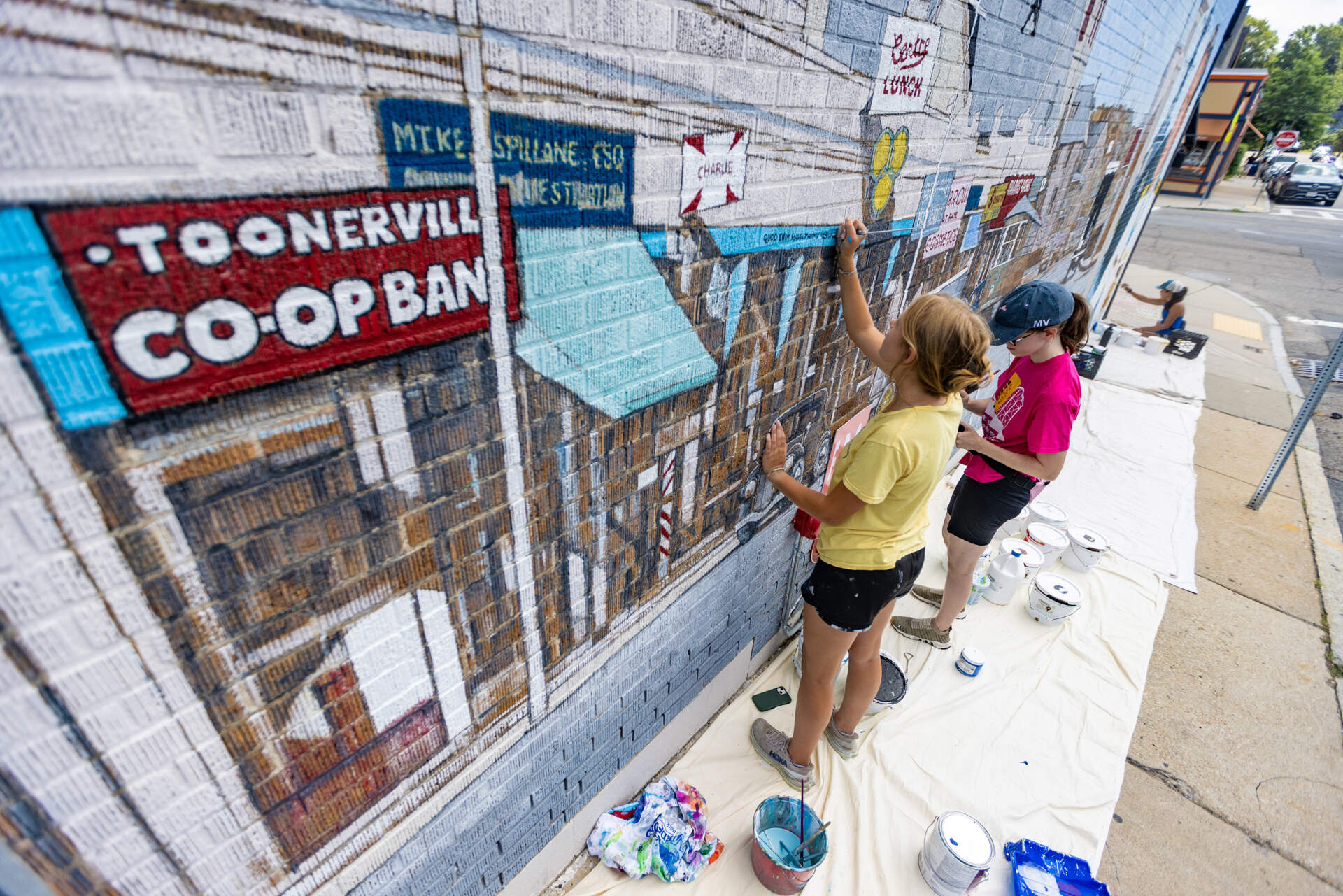 Maia Poremba, Sarah Egan and Laura de Donato do restoration work on the Centre Street mural on the Boston Ale House wall in West Roxbury. (Jesse Costa/WBUR)