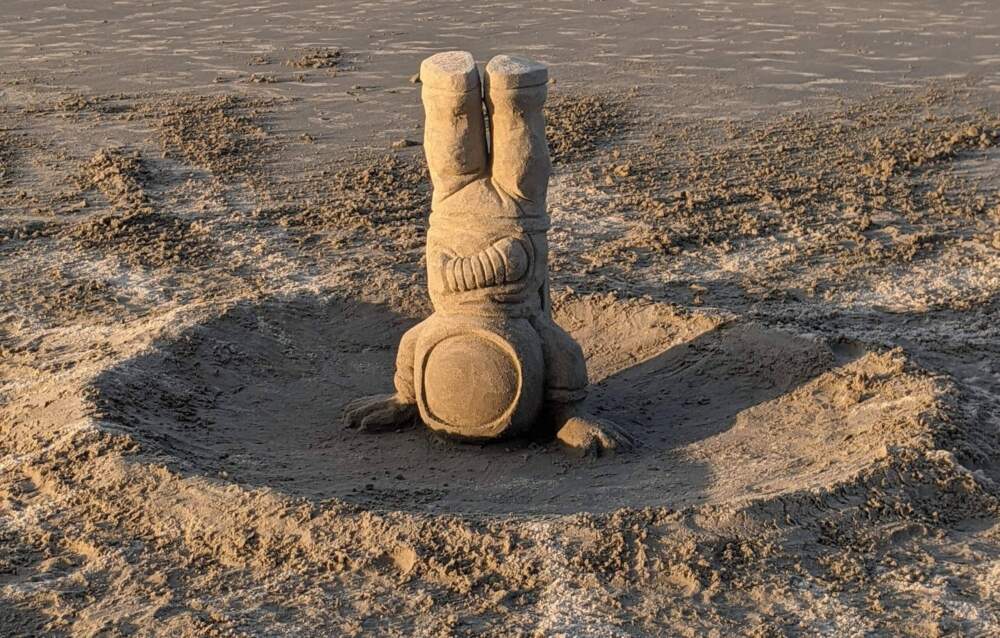 An astronaut carved out of sand by Gary White does a headstand on Nahant Beach. (Courtesy of Gary White)