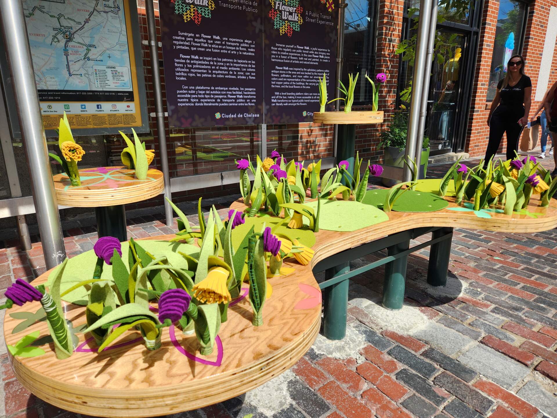 A bench filled in with flowers has been placed at the bus shelter located on Broadway and 3rd Street in Chelsea as part of the &quot;Flower Walk&quot; installation unveiled Aug. 22, 2023. (Andrea Perdomo-Hernandez/WBUR)