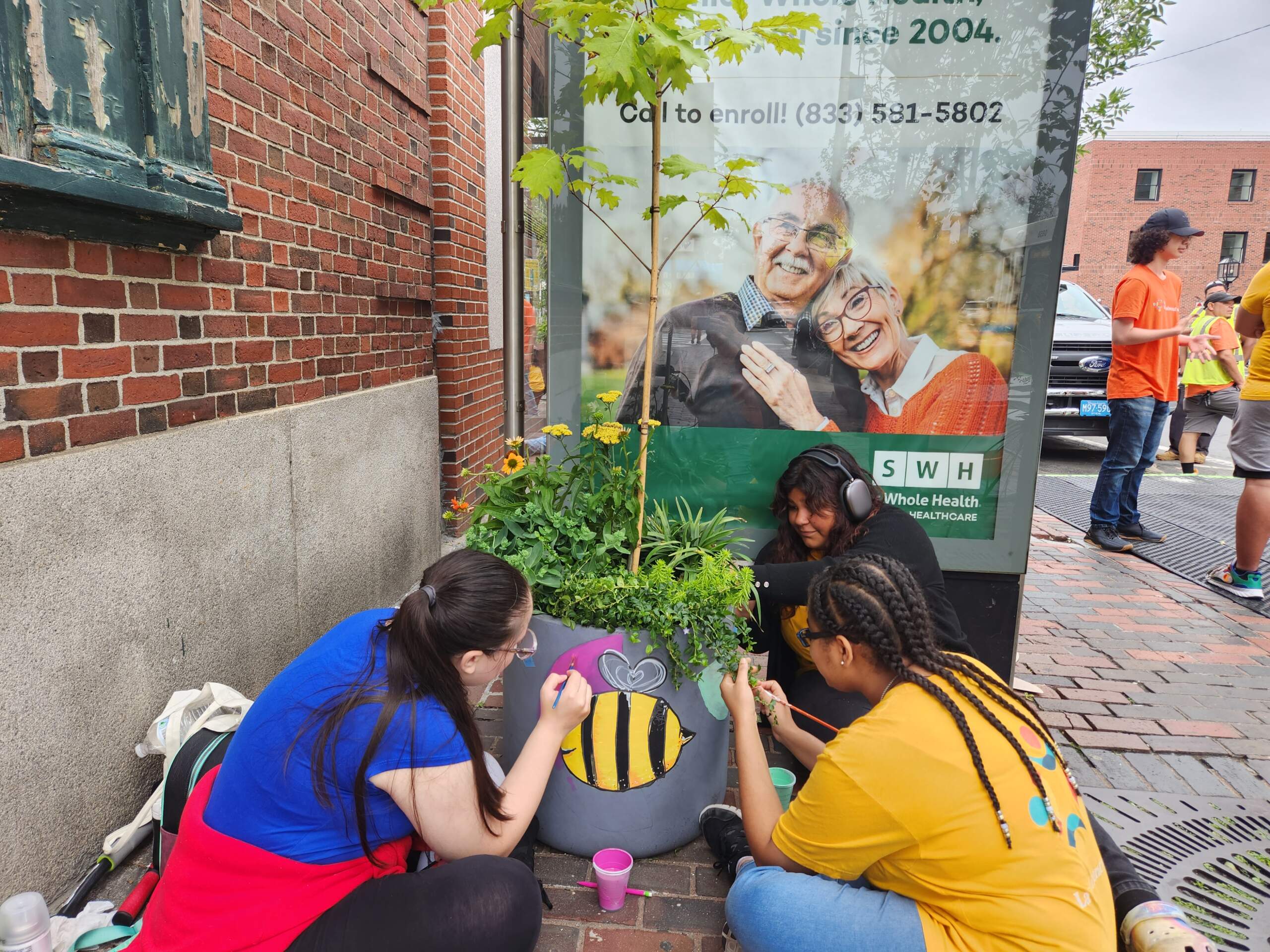 Emily Velasquez, 18, Tinsae Haile, 15, and Rachel Godoy, 15 are members of La Colaborativa's Youth Jobs Summer 2023 program. They paint a planter that's part of the "Flower Walk" art installation in Chelsea. (Andrea Perdomo-Hernandez/WBUR)