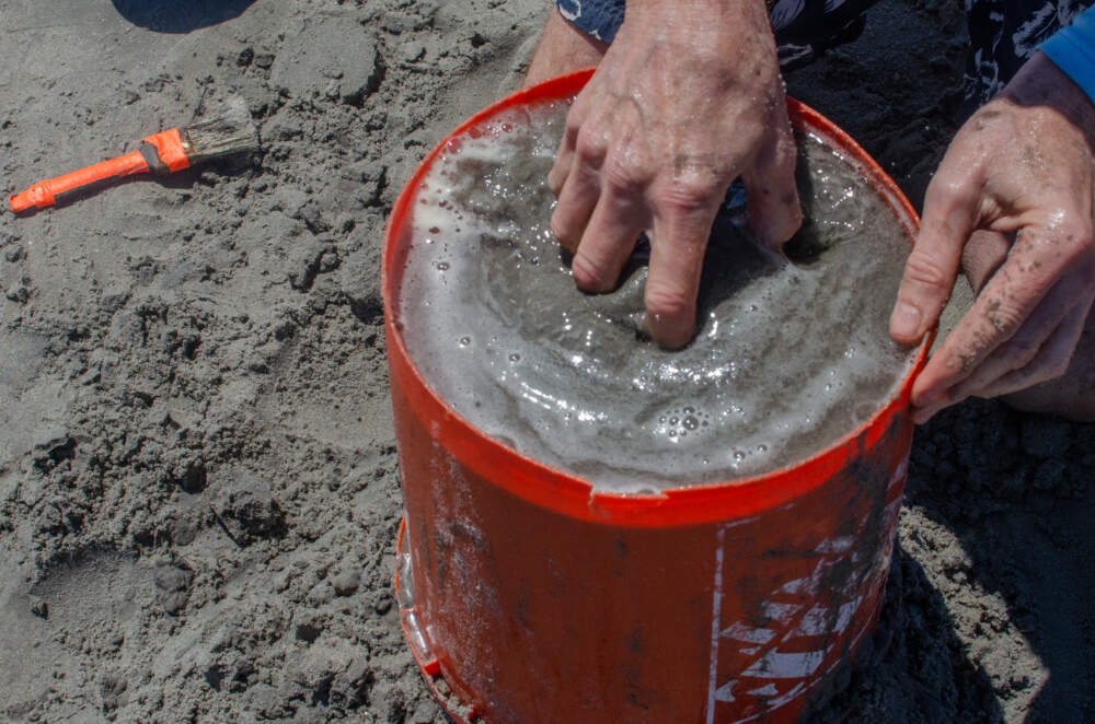 Gary White mixes water and sand in a bucket on Nahant Beach. (Sharon Brody/WBUR)
