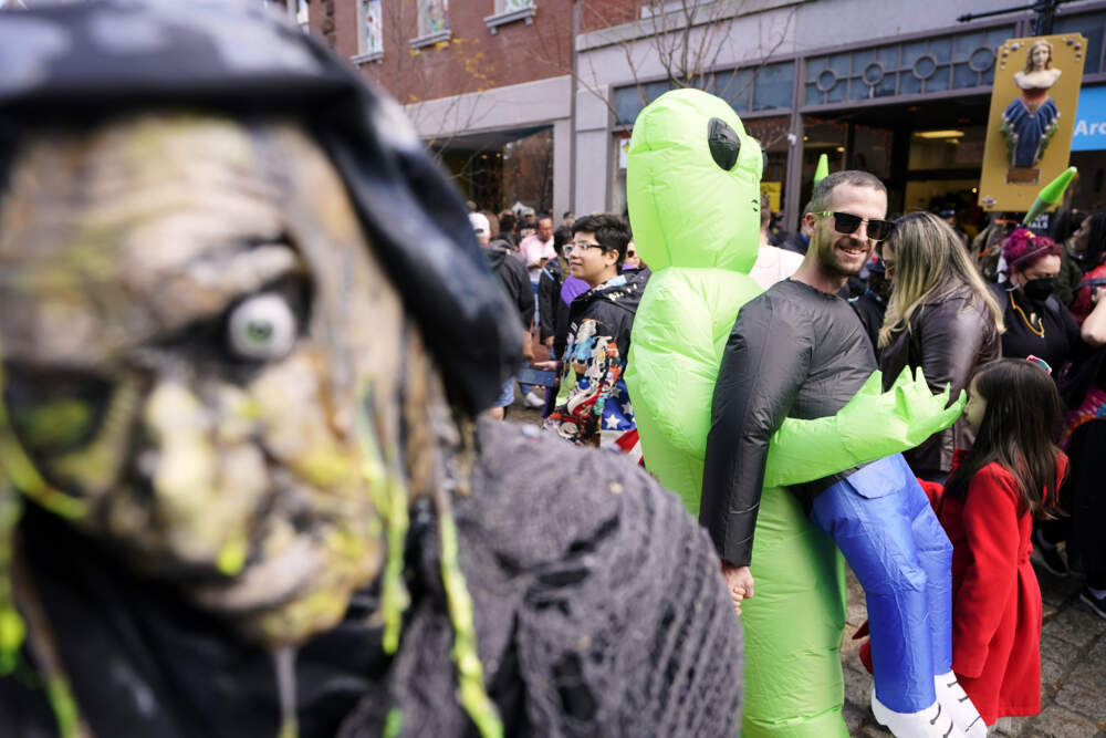 People dressed in a variety of costumes walk past a scary figurine posted in front of a store, left, as they promenade through downtown Salem, Mass., on Halloween. (Steven Senne/AP)