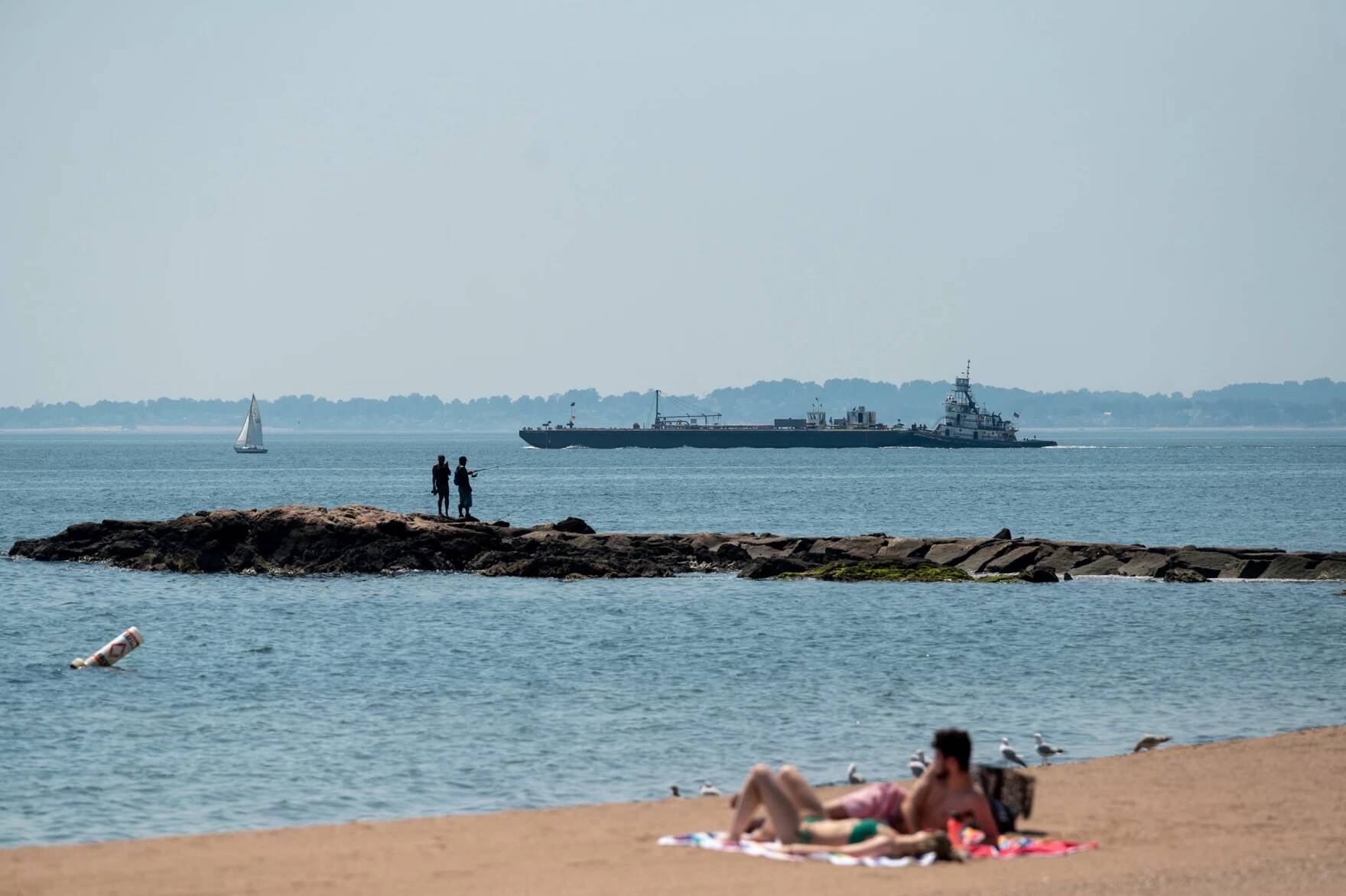 New Haven residents take refuge from the August heat by the waterside at Lighthouse Point Park as boats leave the nearby harbor in 2022. (Ryan Caron King/Connecticut Public Radio)