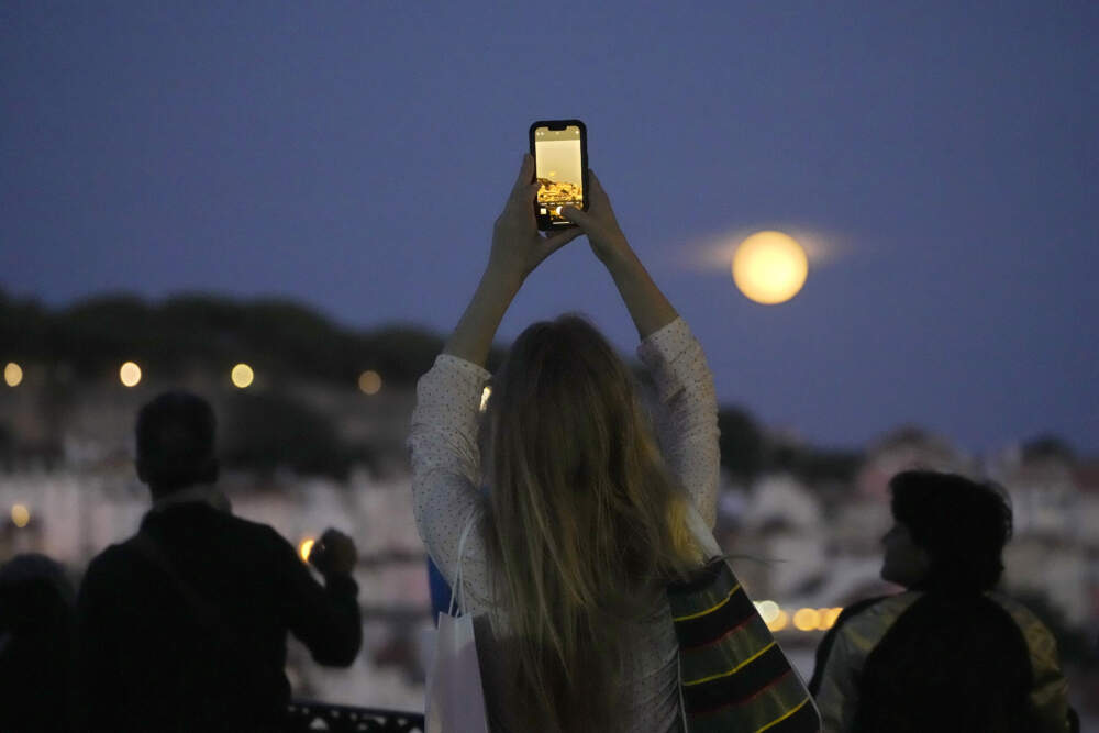 A woman takes pictures of the supermoon rising above Lisbon, Wednesday, Aug. 30, 2023. (Armando Franca/AP)