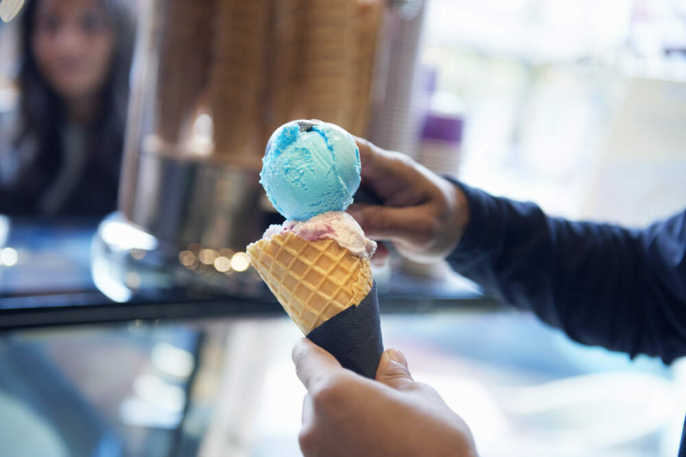 A man scoops ice cream onto a cone. (We Are/Getty Images)