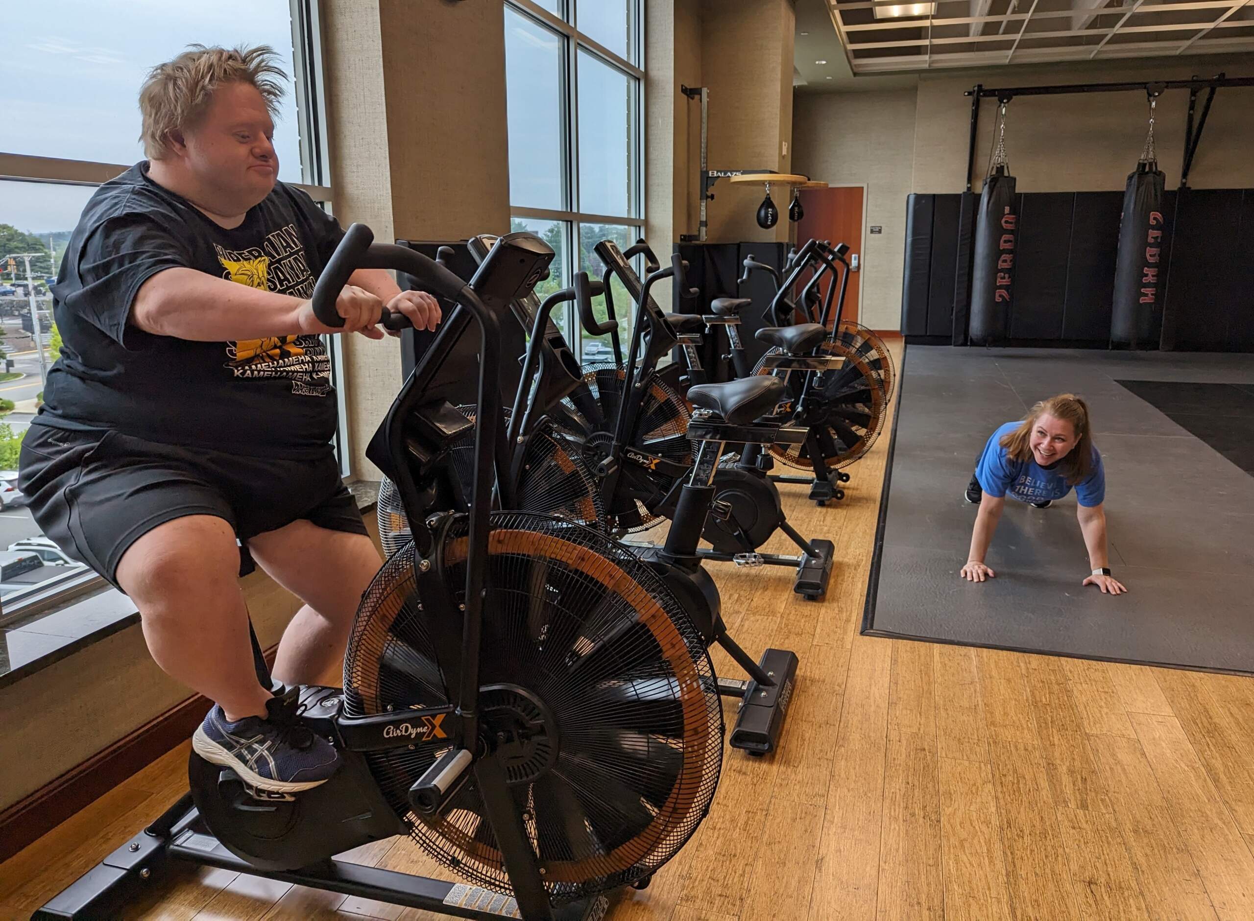 Jason Silverman uses the exercise bike at Life Time in Framingham, while his friend, Melissa Mills, does stretches on the floor. (Priyanka Dayal McCluskey/WBUR)