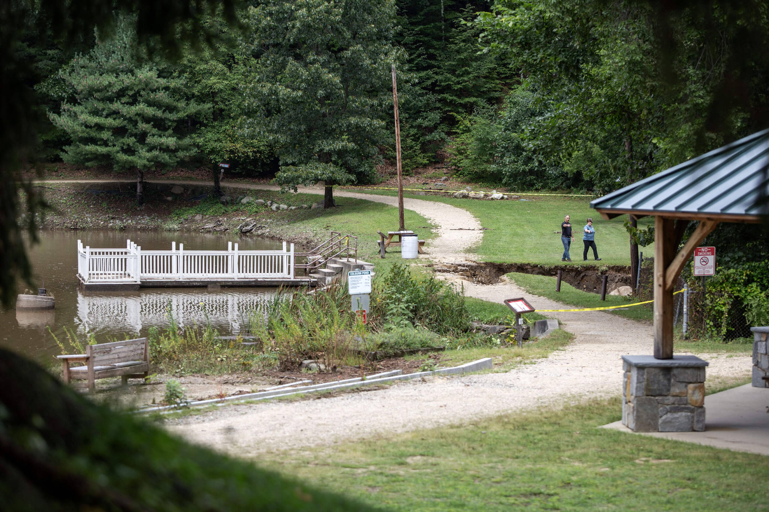 Officials inspect an area behind a dam in Barrett Park in Leominster that sustained damaged from the flooding. (Robin Lubbock/WBUR)
