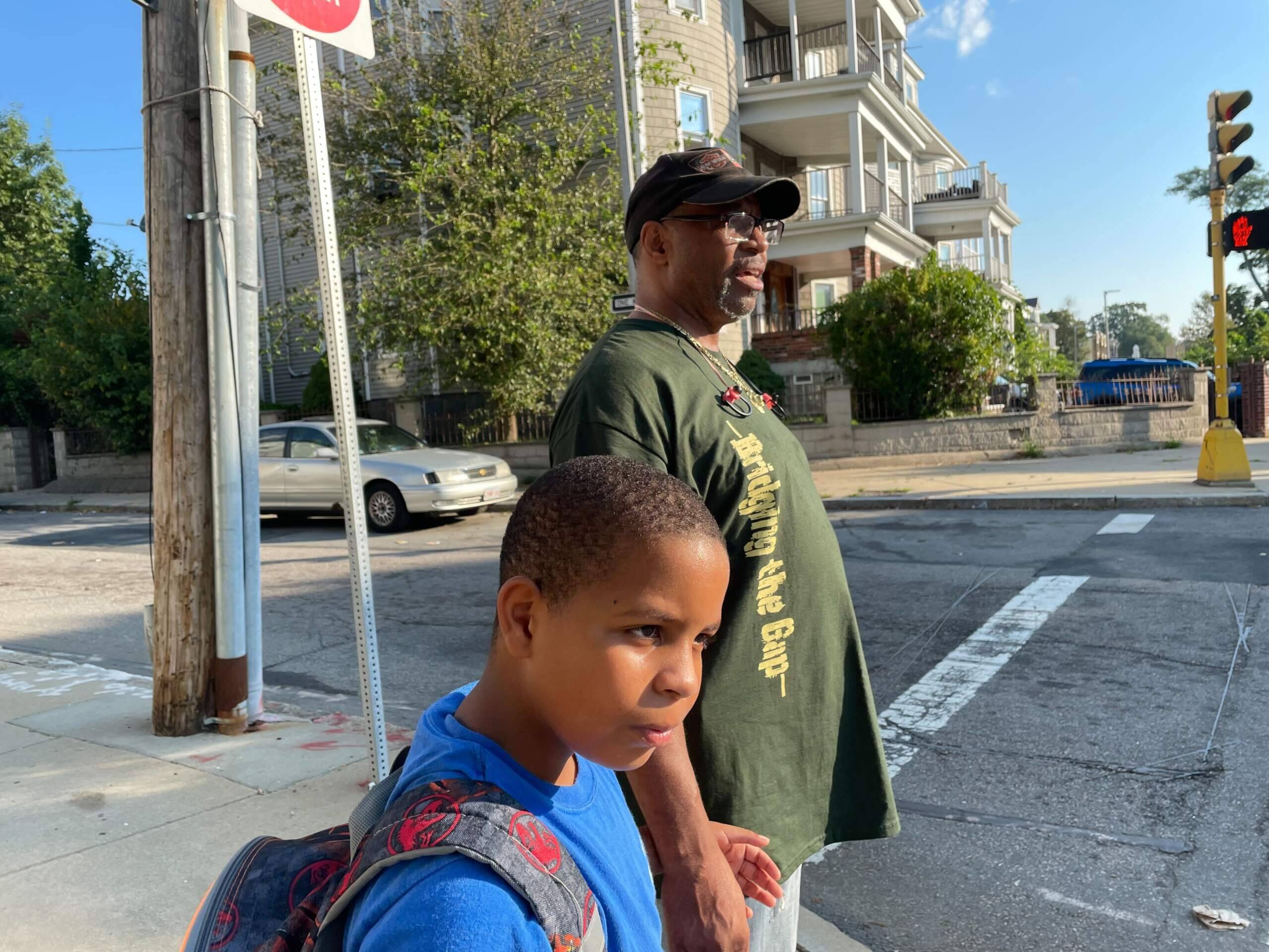 Fitzgerald Allen and his grandson, Harley, wait for a school bus that's running late in Mattapan on the first day of school. (Max Larkin/WBUR)