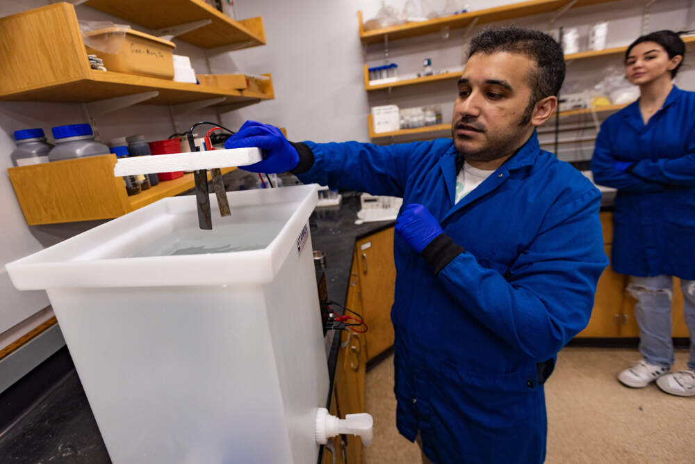 Amir Taqieddin. Shown here as a PhD student at Northeastern University working in the lab of Akram N Alshawabkeh, but he has since graduated. Taqieddin is demonstrating a prototype of a device that could float on the surface of the ocean and deliver a steady dose of iron for iron enhancement experiments. (Jesse Costa/WBUR)