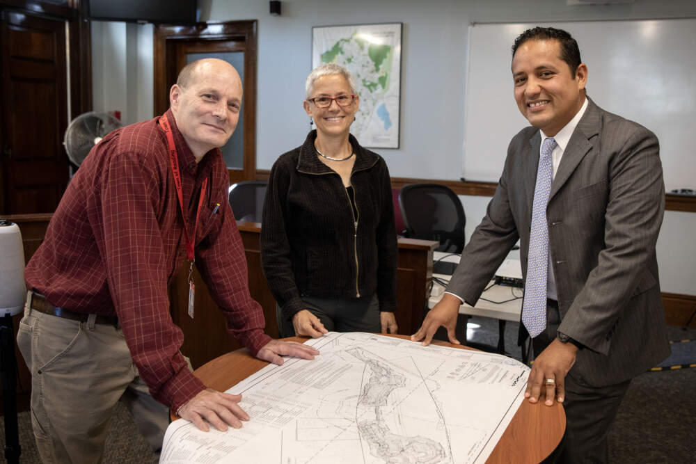Reading Conservation Administrator Chuck Tirone, Mystic River Watershed Association Senior Policy Advisor Julie Wormser and Reading Town Manager Fidel Maltez look over plans for a wetland construction project in the Maillet, Sommes and Morgan conservation area. (Robin Lubbock/WBUR)