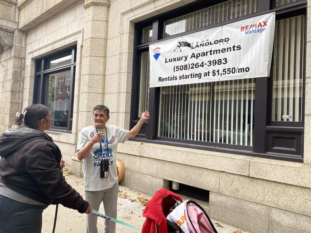 New Bedford resident Millie Padilla mocks a sign advertising luxury housing in downtown New Bedford. (Simón Rios/WBUR)