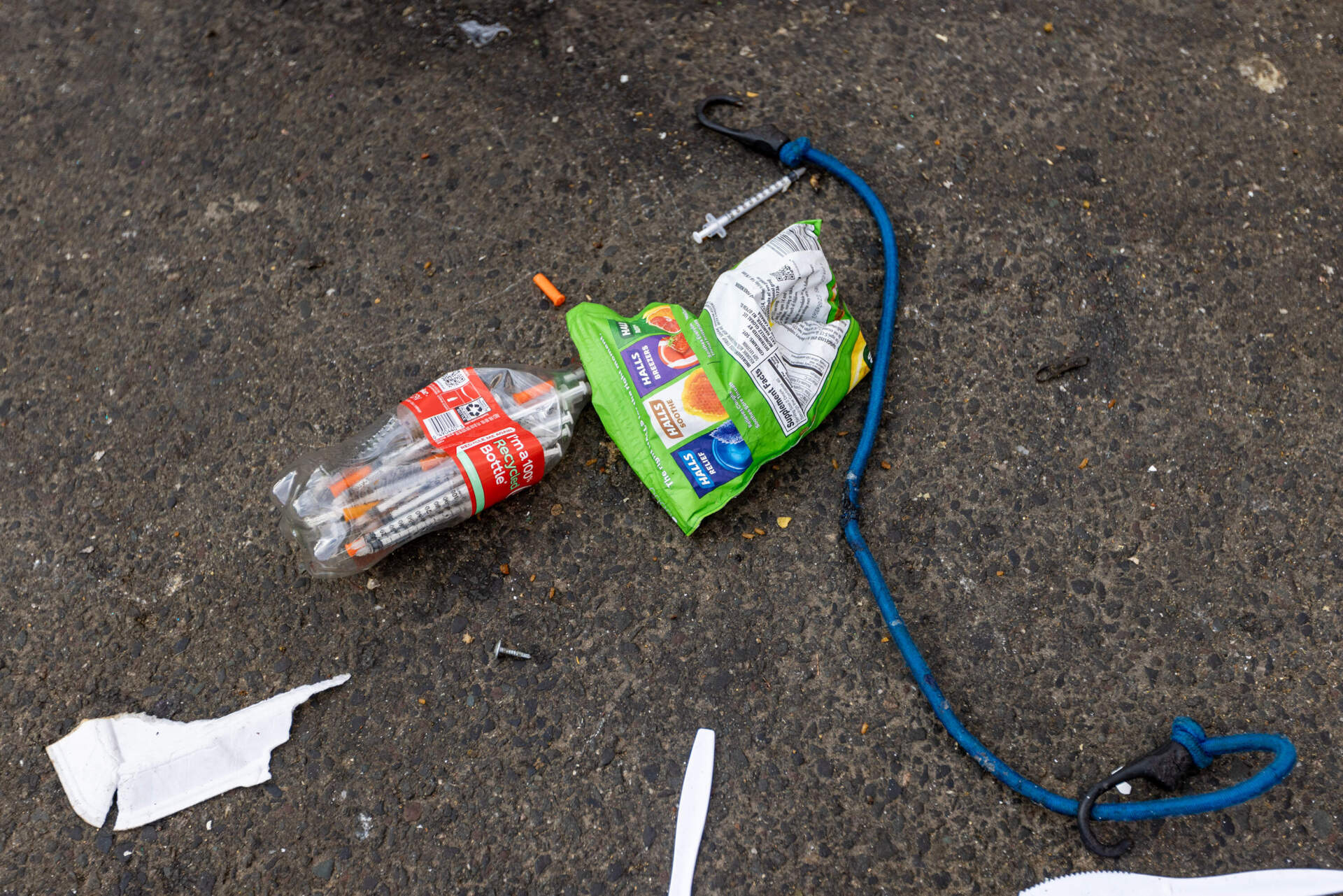 A bag and Coca-Cola bottle filled with syringes is seen on the ground during the tent encampment removal on Atkinson Street in the area known as &quot;Mass and Cass.&quot; (Jesse Costa/WBUR)