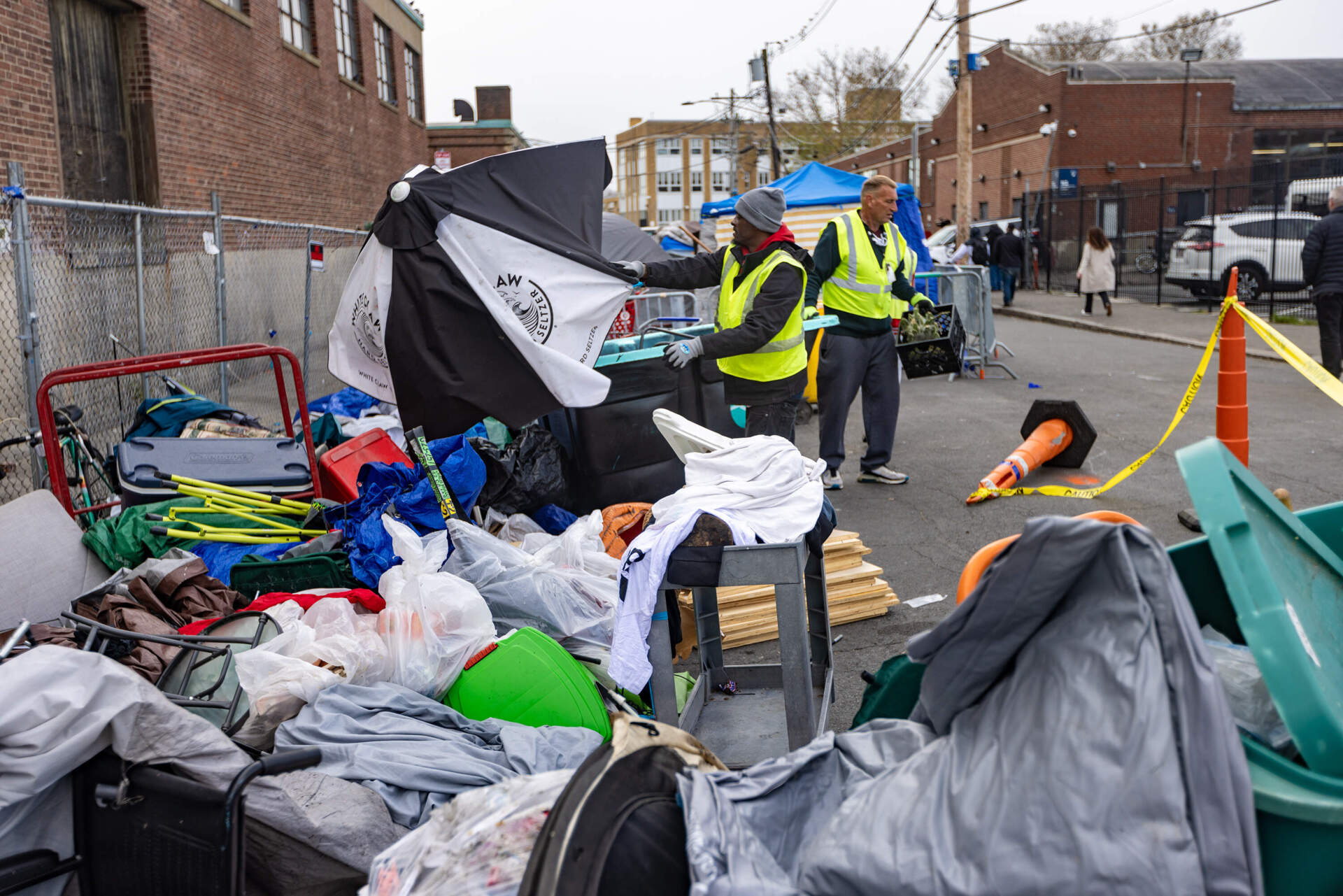 A volunteer from the Newmarket Business Improvement District throws an umbrella away into a large pile of trash. (Jesse Costa/WBUR)