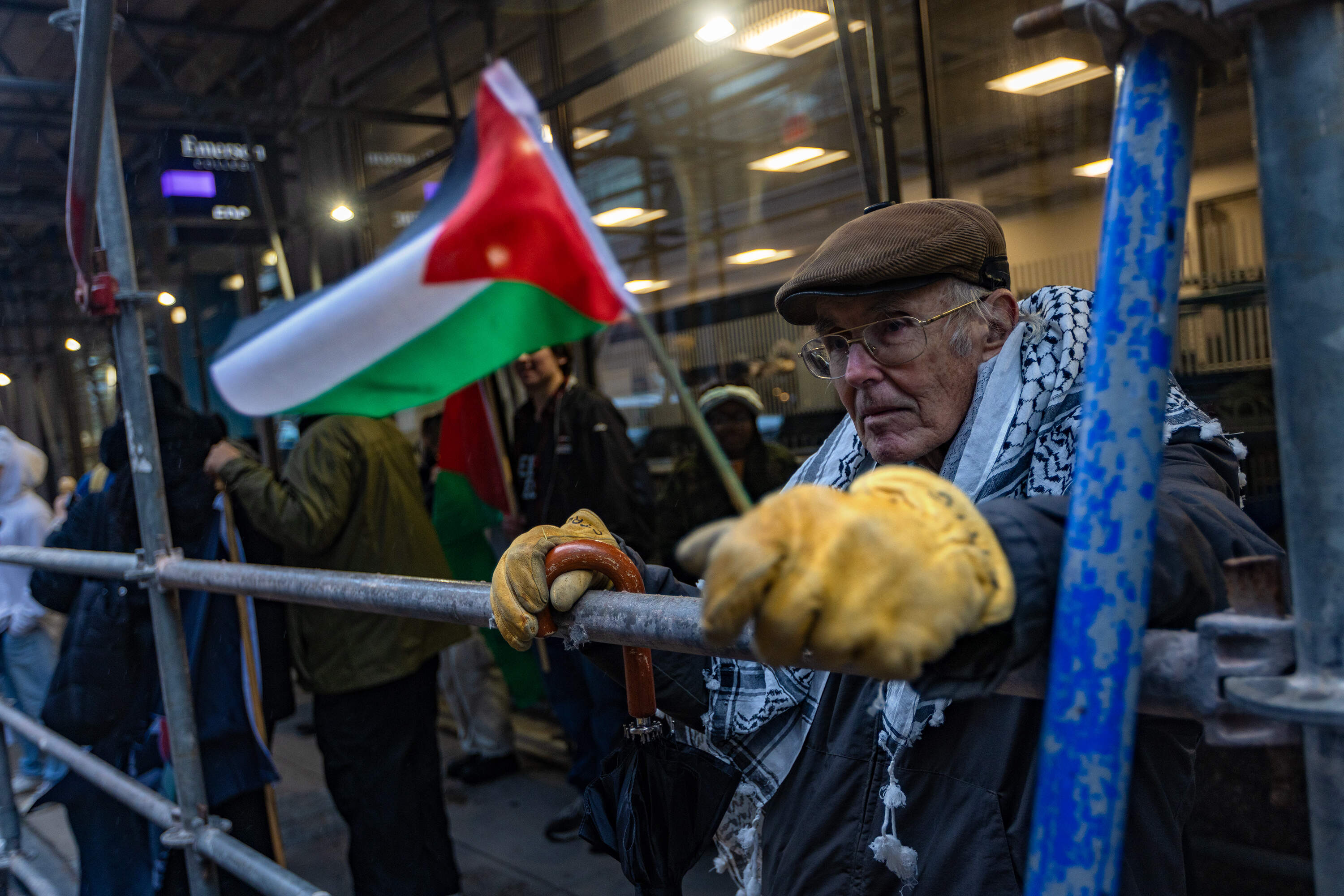 A man holding a Palestinian flag stands with other protesters across the street from the Ritz Carlton Hotel where Vice President Kamala Harris is staying in Boston. (Jesse Costa/WBUR)