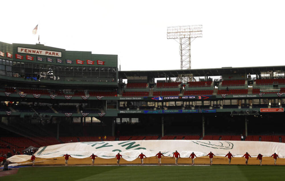 Groundskeepers remove the tarp over the infield at Fenway Park following a rain storm before Game 1 of the World Series baseball game between the Boston Red Sox and Los Angeles Dodgers  in 2018. (Matt Slocum/AP)