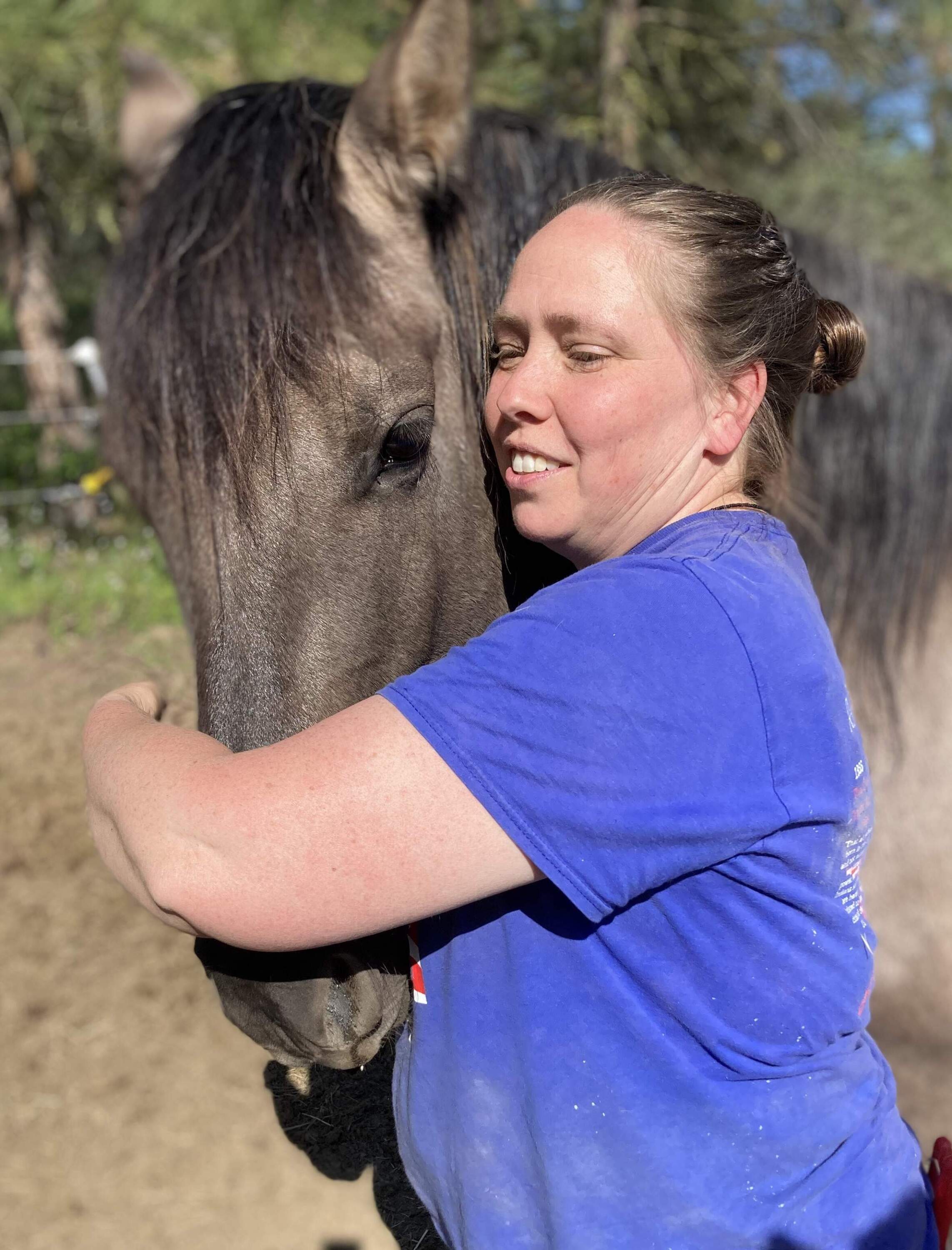 Allison Burke, founder of Spqni Equines in Transition, hugs her mustang, Blue. “He's got a very, very low fear threshold. So he doesn't always let me touch him. It's got to be his idea.” (Ashley Ahearn)