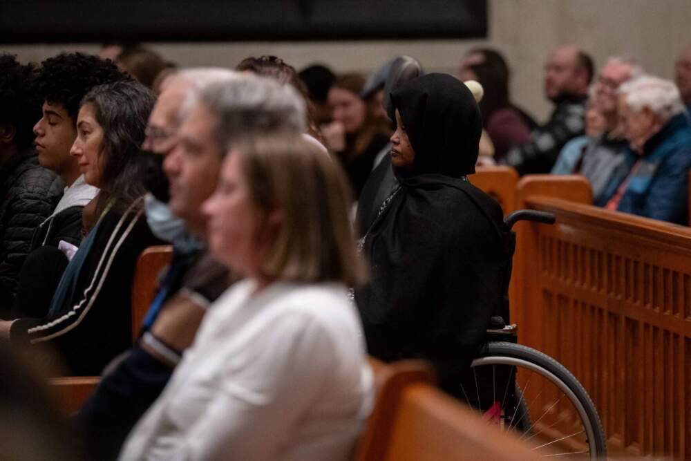 Fowsia Musse, executive director of Maine Community Integration, right, listens to speakers during the OneLewiston Community Vigil in the Basilica of Saints Peter and Paul in Lewiston, Maine. (Raquel C. Zaldívar/New England News Collaborative)