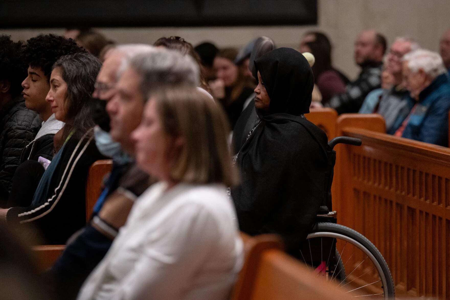 Fowsia Musse, executive director of Maine Community Integration, right, listens to speakers during the OneLewiston Community Vigil in the Basilica of Saints Peter and Paul in Lewiston, Maine. (Raquel C. Zaldívar/New England News Collaborative)