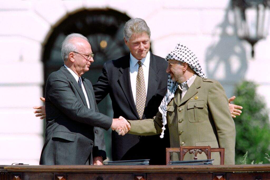 US President Bill Clinton (C) stands between PLO leader Yasser Arafat (R) and Israeli Prime Minister Yitzahk Rabin (L) as they shake hands for the first time, on September 13, 1993 at the White House in Washington DC, after signing the historic Israel-PLO Oslo Accords on Palestinian autonomy in the occupied territories. AFP PHOTO J.DAVID AKE (Photo by J. DAVID AKE / AFP) (Photo by J. DAVID AKE/AFP via Getty Images)
