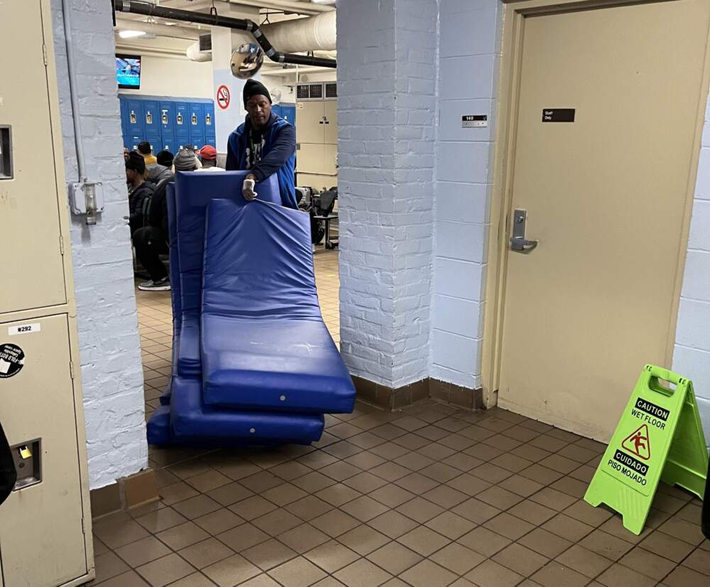 A Pine Street Inn employee moves sleeping mats into a room that will be used as overflow shelter space. (Lynn Jolicoeur/WBUR)