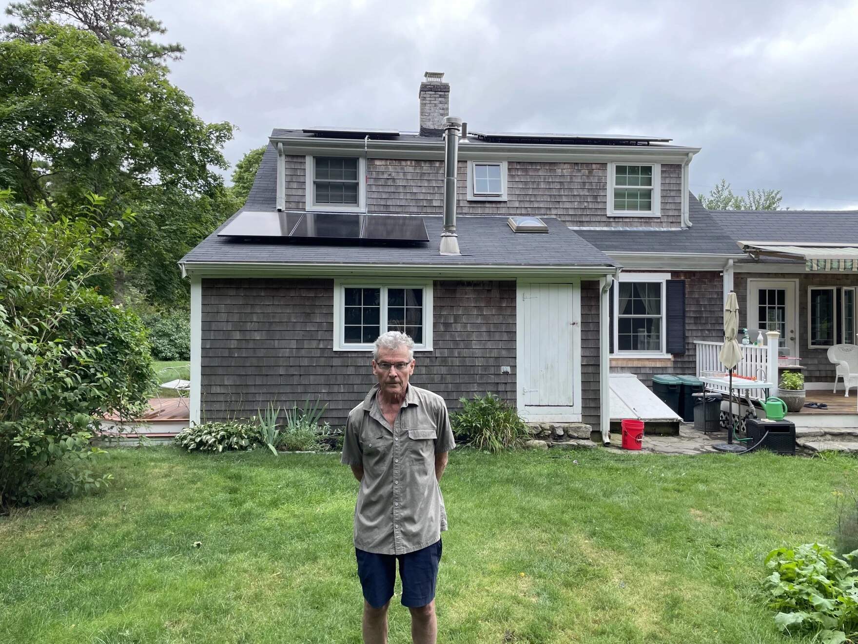 John Beach stands in his backyard in Yarmouth, where he can see his newly installed solar panels. (Eve Zuckoff/CAI)