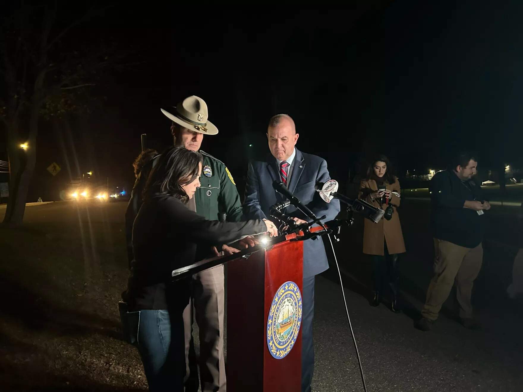 Left to right: New Hampshire Division of Homeland Security and Emergency Management Community Outreach Coordinator Vanessa Palange, New Hampshire State Police Director Mark Hall and New Hampshire Safety Commissioner Robert Quinn at a Friday evening briefing on the shooting in Concord. (Mara Hoplamazian/NHPR)