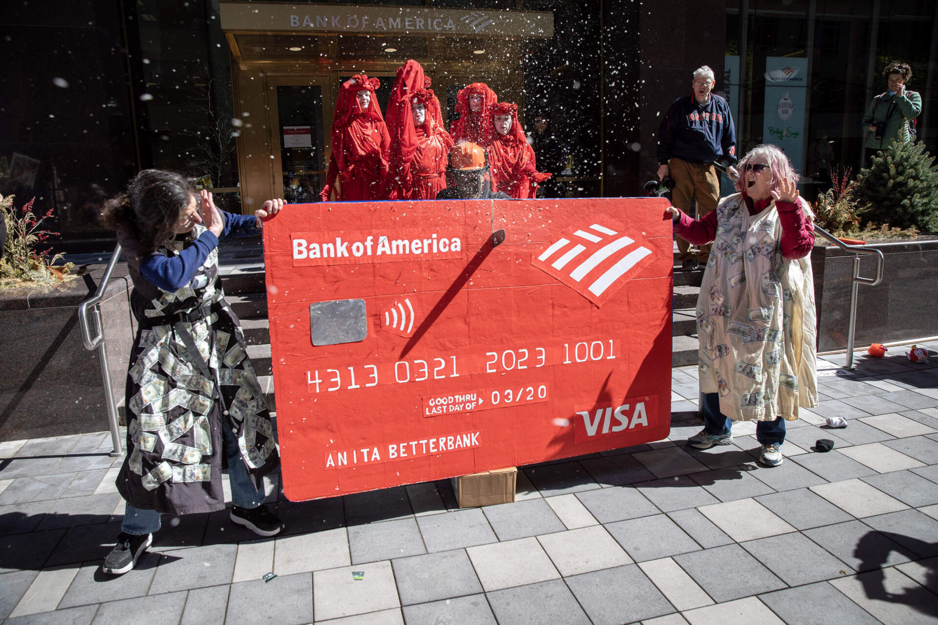 Sawdust flies as protesters chop up a giant credit card with a solar powered chainsaw in front of the Bank of America in downtown Boston. (Robin Lubbock/WBUR)