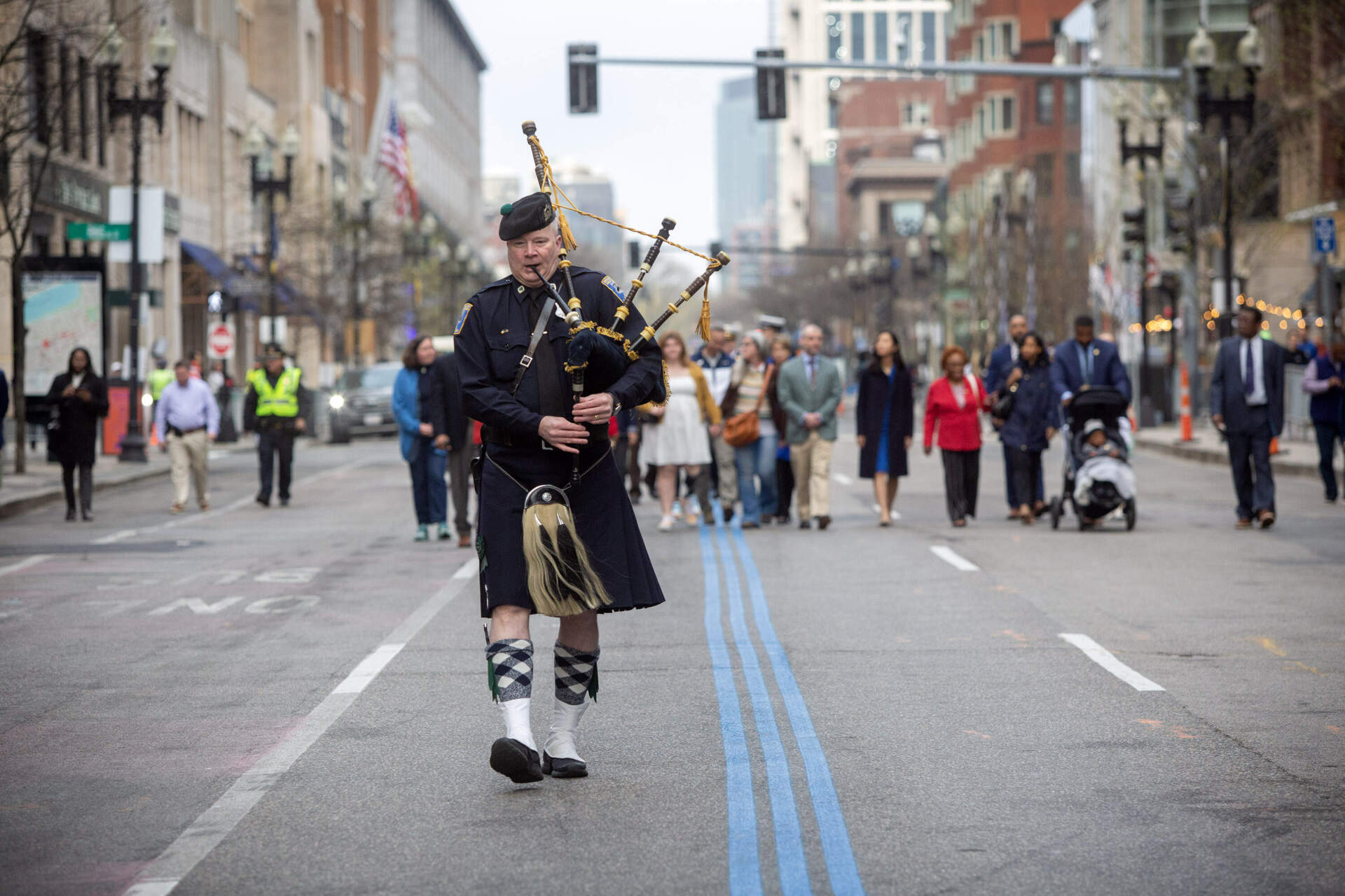 A piper leads Gov. Maura Healey and Boston Mayor Michelle Wu along Boylston Street at a remembrance with families who lost loved ones at the 2013 Boston Marathon bombings. (Robin Lubbock/WBUR)