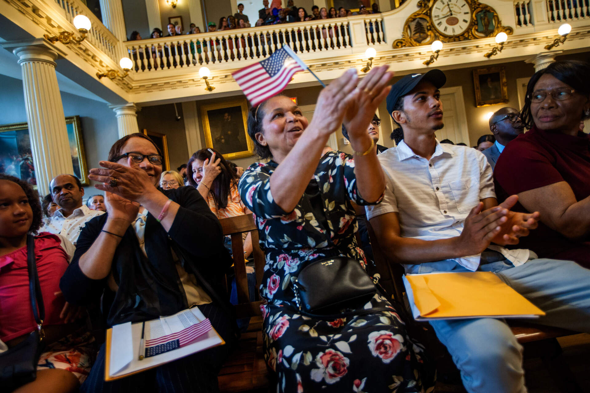 Alina Gomes, originally from Cape Verde, claps while holding an American flag during a naturalization ceremony at Faneuil Hall. (Jesse Costa/WBUR)