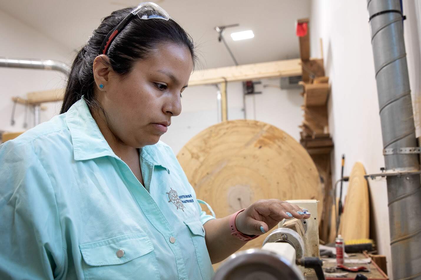 Christina Fuller inspects her work on a boat wheel spoke at South Shore Boatworks in Carver. (Robin Lubbock/WBUR)