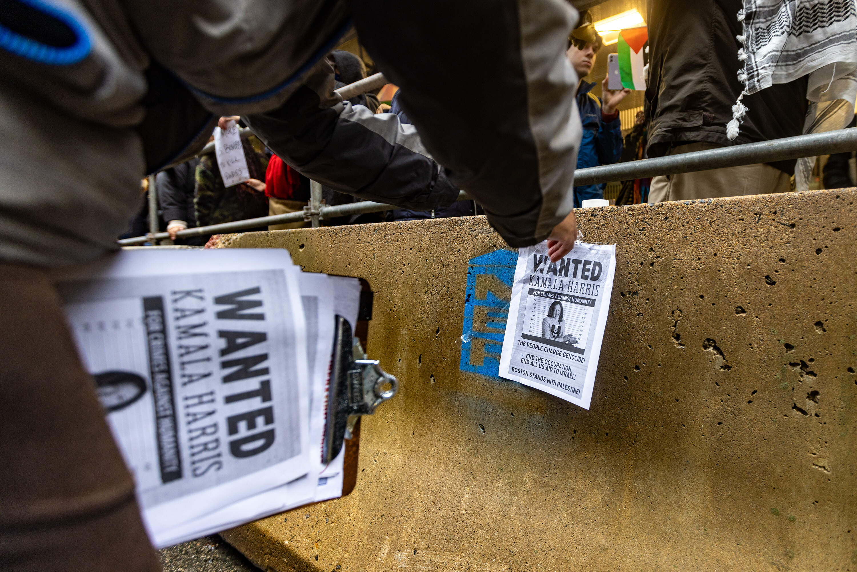 A protestor tapes a wanted poster with Kamala Harris on it across the street from the Ritz-Carlton Hotel during a pro-Palestinian rally. (Jesse Costa/WBUR)