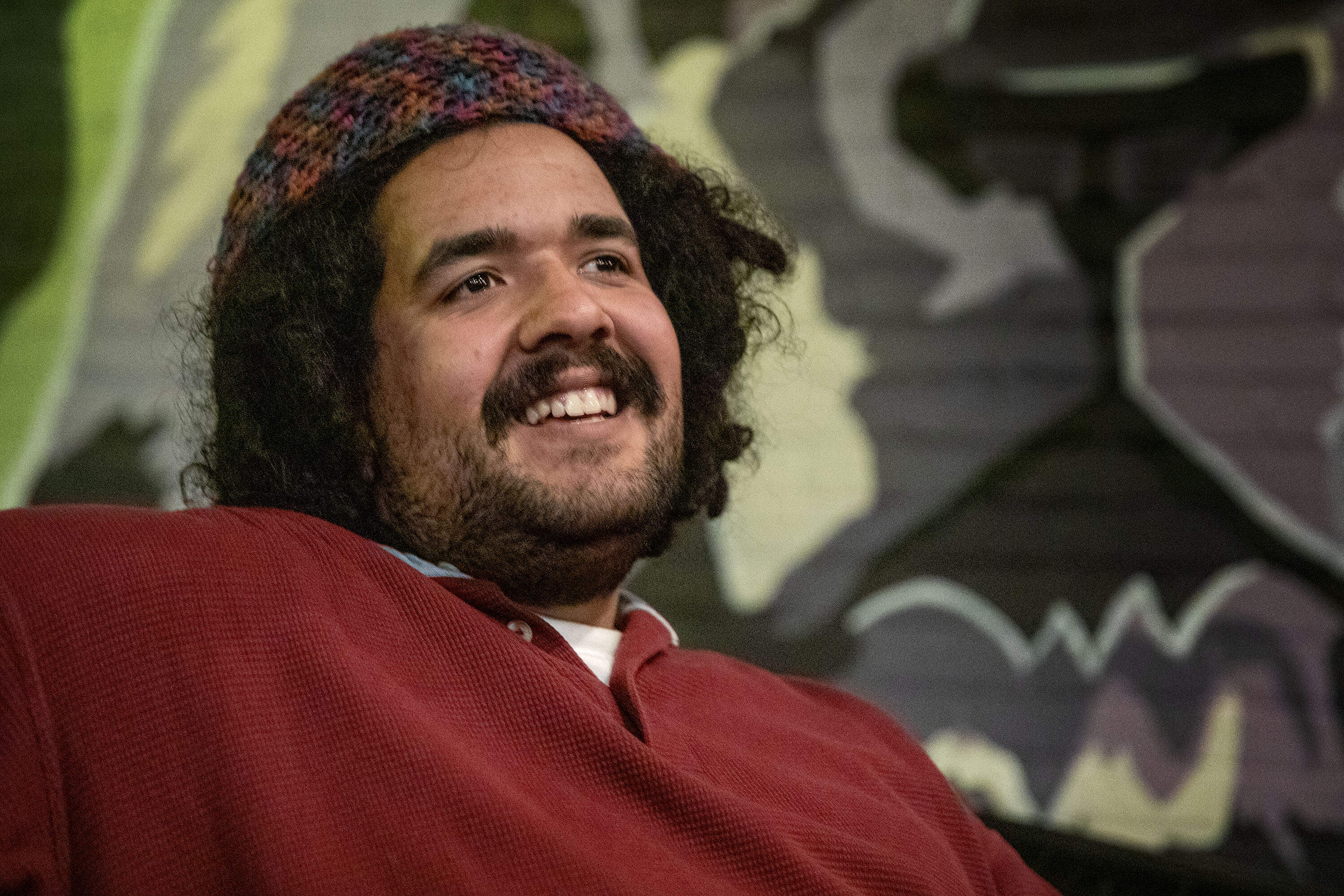A seated man, leans back, with a smile on his face.