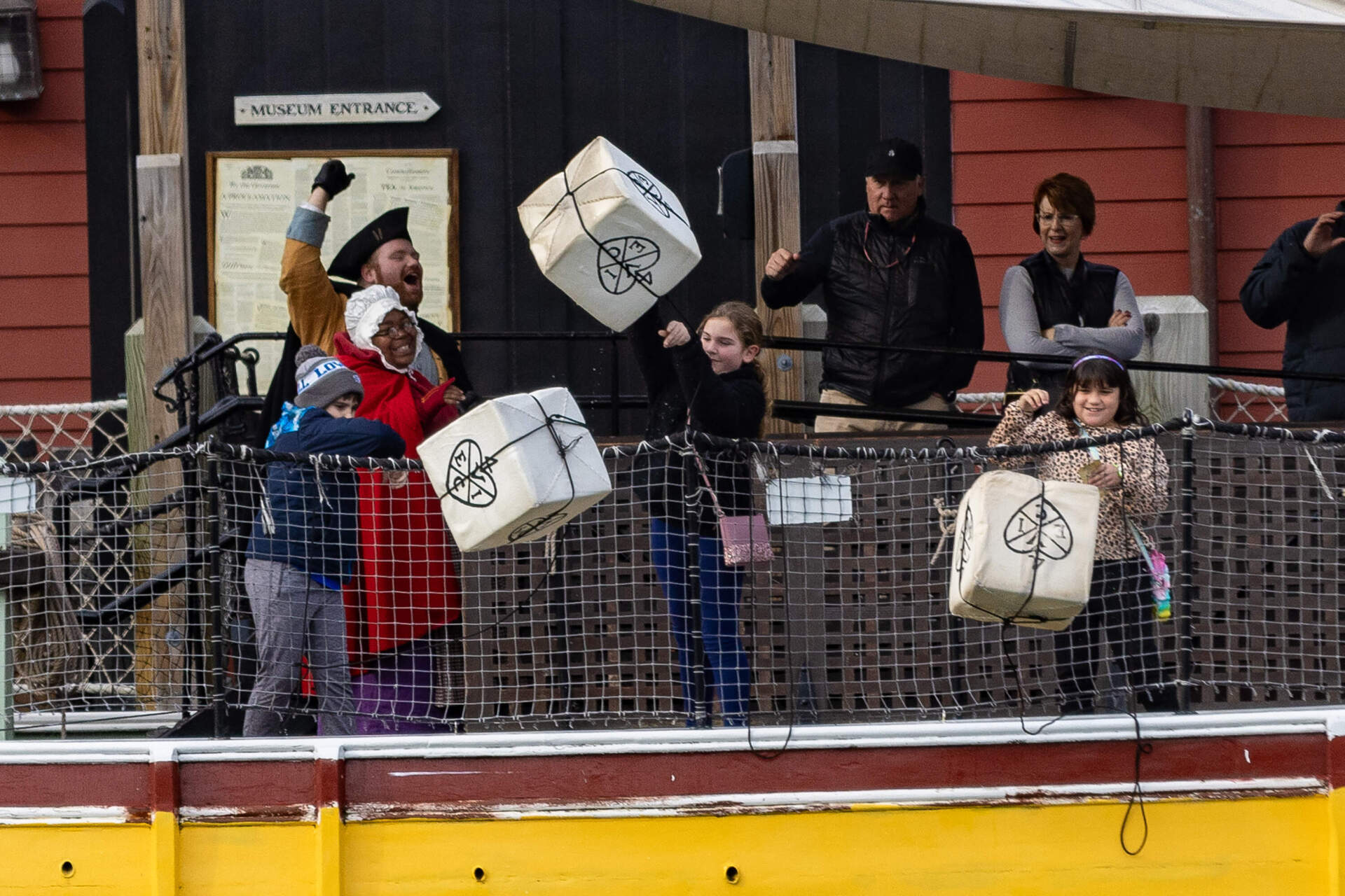 Three young museum goers toss crates with the emblem of the East India Company overboard into the Fort Point Channel from the merchant vessel Eleanor during a visit to the Boston Tea Party Museum. 