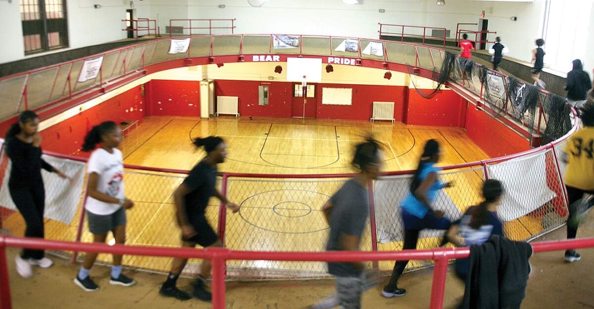 With ‘Bear Pride’ in the background, TechBoston Academy indoor track athletes practice on a dilapidated oval track above the old gym in their building – the former Dorchester High School. (Seth Daniel/Dorchester Reporter)