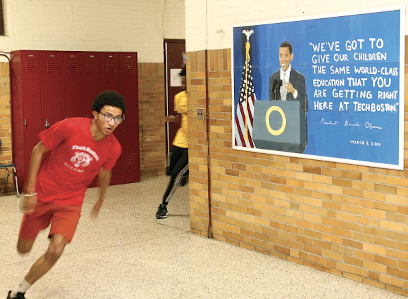 Kalvin Johnson turns a corner in a hallway at TechBoston Academy during track practice last Friday afternoon, passing by a tribute to former President Barack Obama who visited the school in 2011 and cited its “world-class education” program. (Seth Daniel/Dorchester Reporter)