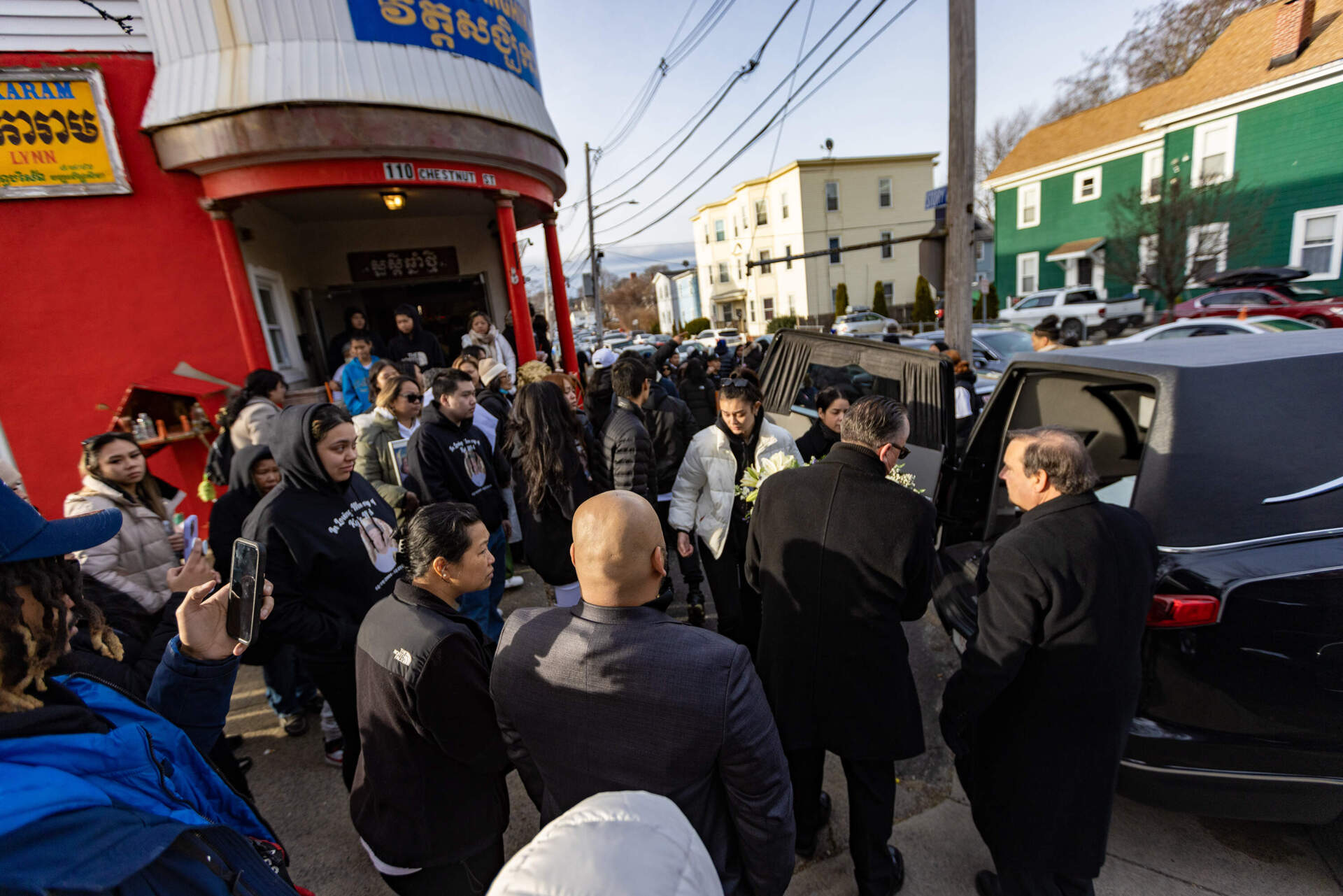 Mourners gather outside a Buddhist temple in Lynn after the casket with the body of Kyle Mel is placed into a hearse that will drive to a burial site in Peabody. (Jesse Costa/WBUR)